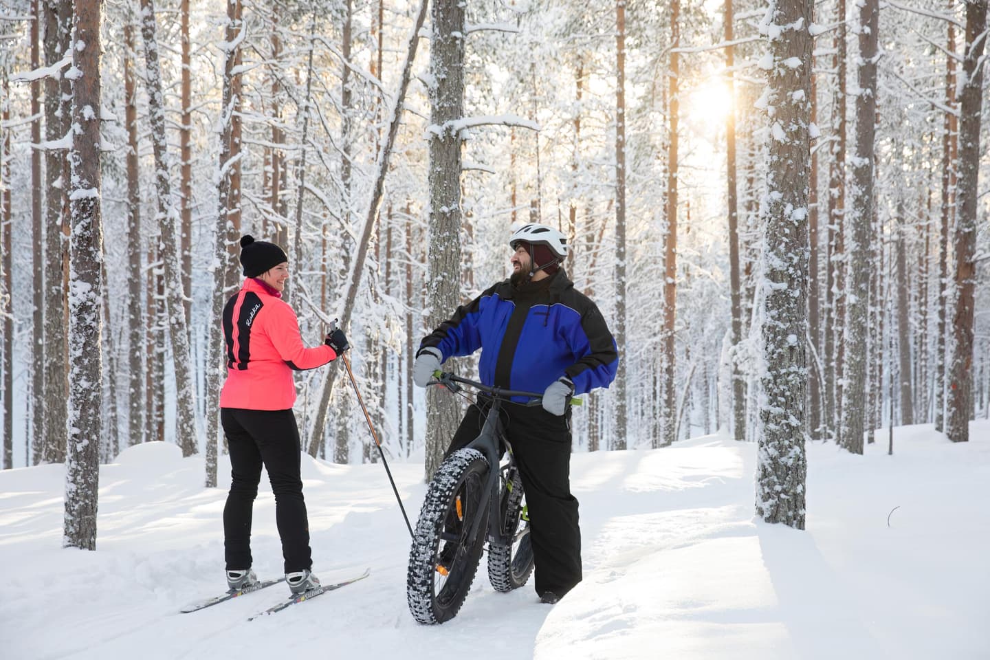 Image: Katri Lehtola / Keksi A cross-country skier and a fatbike cyclist have stopped to chat on a trail in a snowy forest.