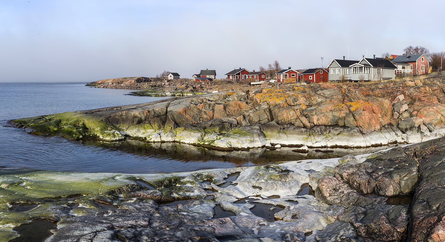 Image: Jari Kostet Kallioita meren rannalla, taaempana punaisia rakennuksia