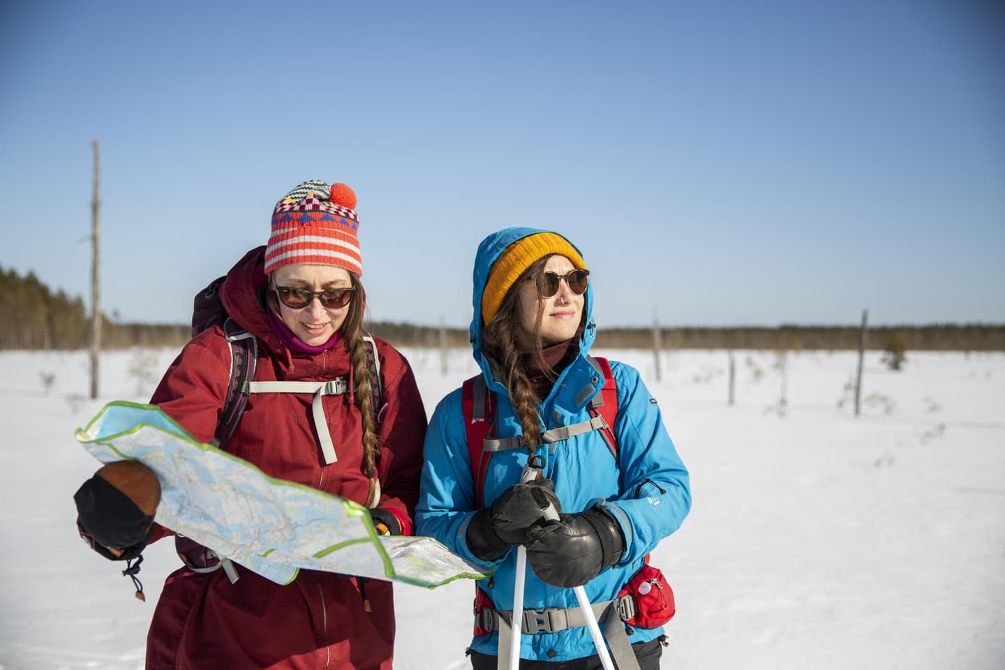 Bild: Saara Lavi Två skidåkare. Den ena läser en karta och den andra har stängt ögonen och vänt ansiktet mot solen.