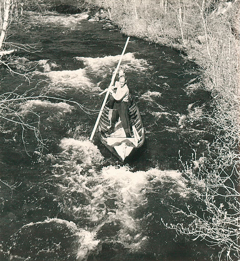 Kuva: Sirkka Saastamoinen Vanha mustavalkokuva, jossa on kaksikoskenlaskijaa vanhassa puuveneessä. Toinen pitelee pitkää puista sauvaa ja toinen ohjaa perästä.