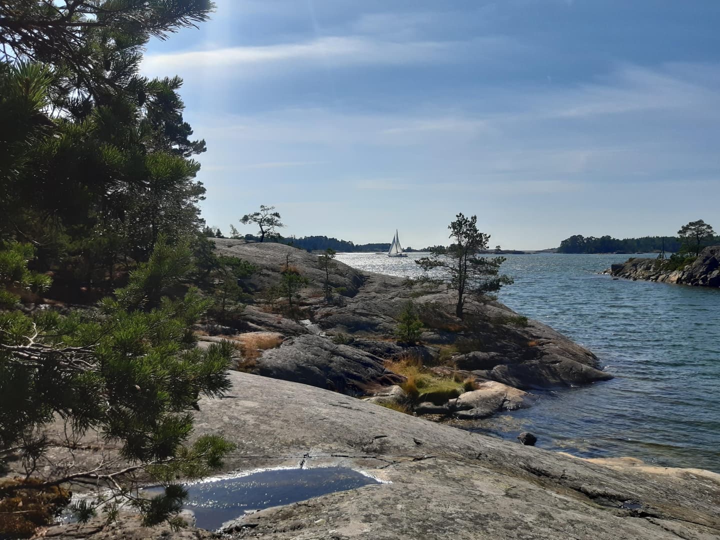 Image: Kirsi Nikkola A bay, a rocky shore with a few trees, a sailboat and islands in the background.