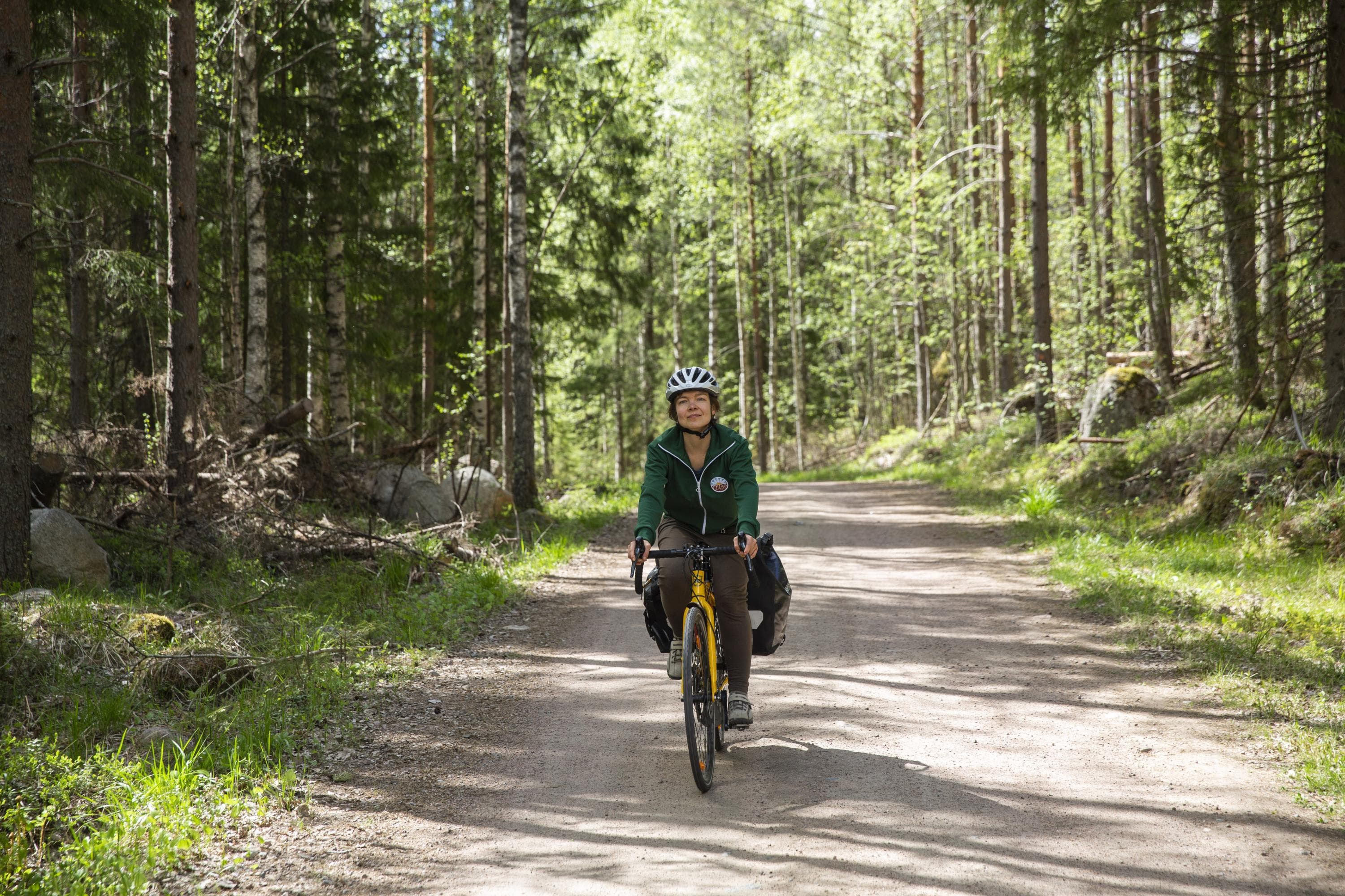 Image: Saara Lavi A cyclist rides on a gravel road surrounded by forest. The bike has full panniers on the rack.