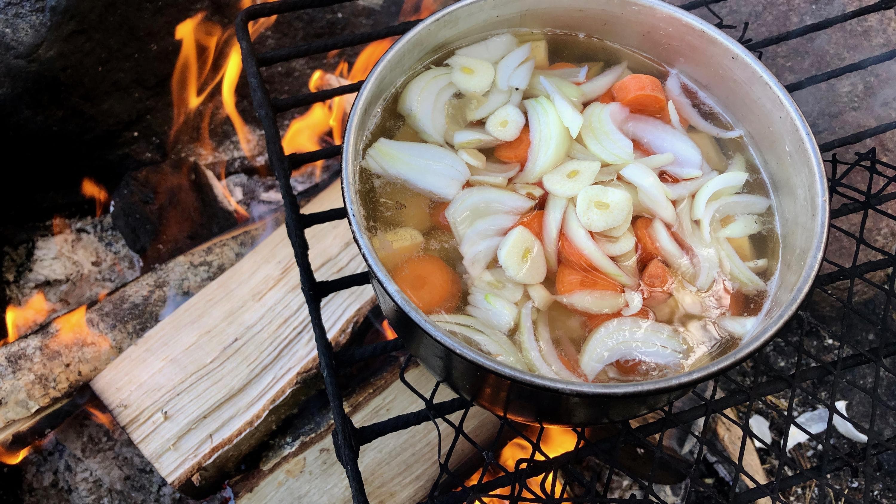 Kuva: Jussi Halttunen Nuotiotulella kasvikset kiehumassa kattilassa.