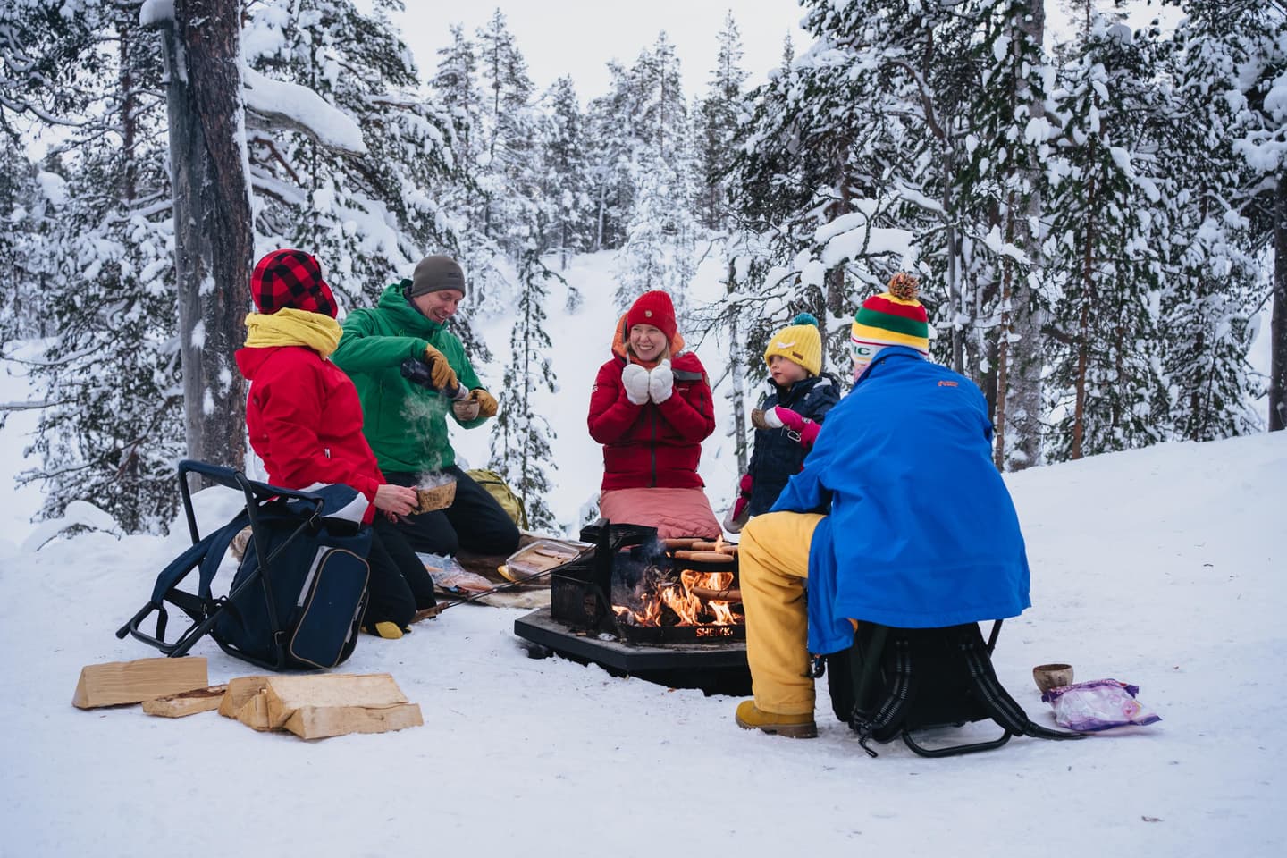 Bild: Jaakko Posti Människor sitter vid lägerelden. I bakgrunden ett snöigt skogslandskap.