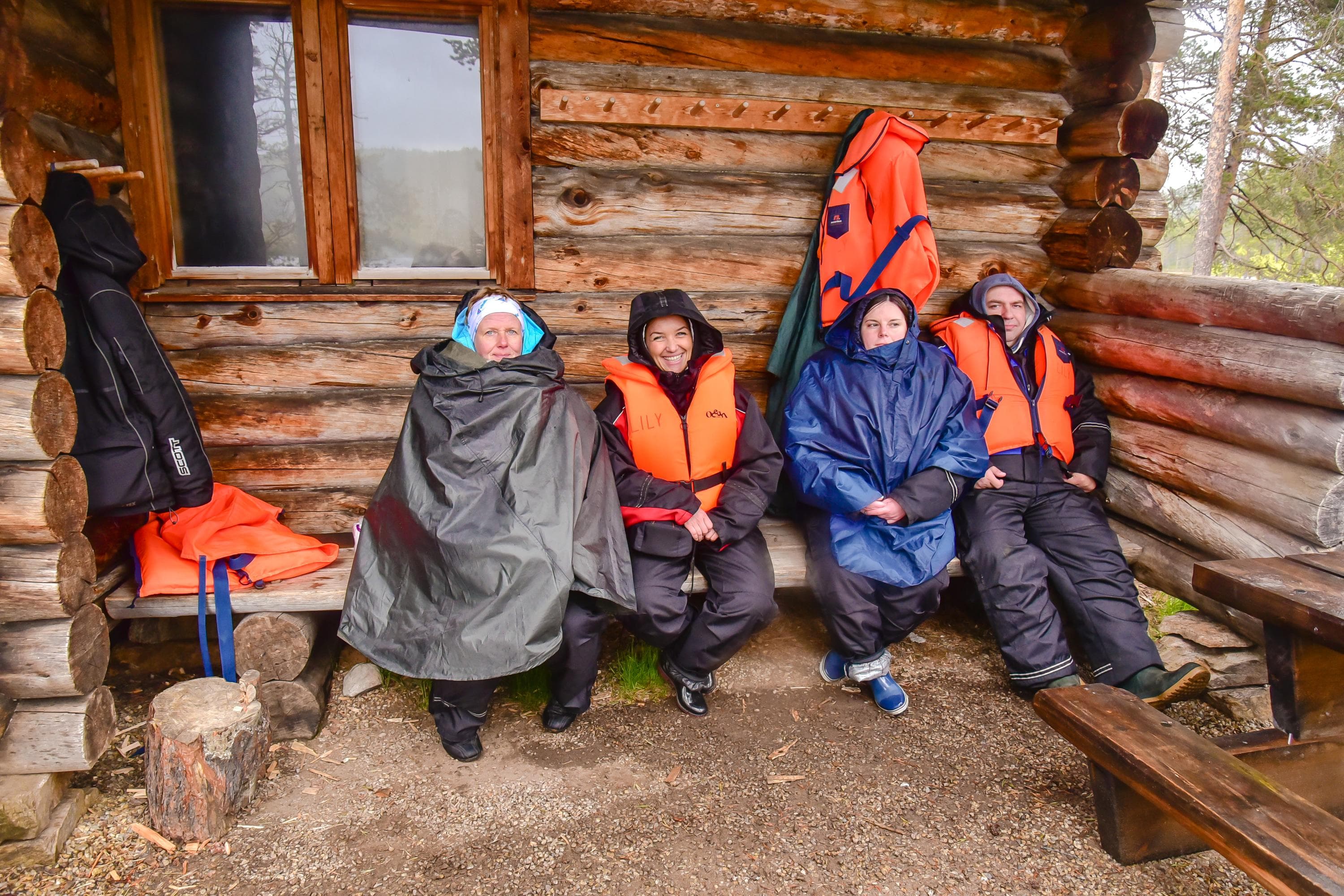 Bild: Tatiana Yakovleva Fyra vandrare sitter bredvid varandra på en träbänk. De har gummistövlar och regnkläder på sig. Två av dem har flytvästar.
