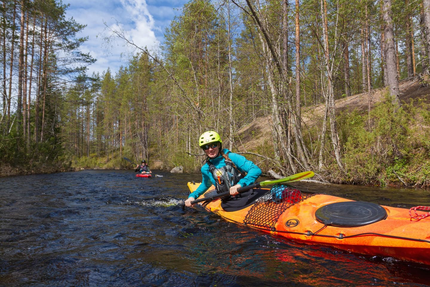 Kaksi melojaa keväisellä joella. Lähikuvassa oleva meloja kallistaa melallaan itseään lähemmäs vesirajaa.