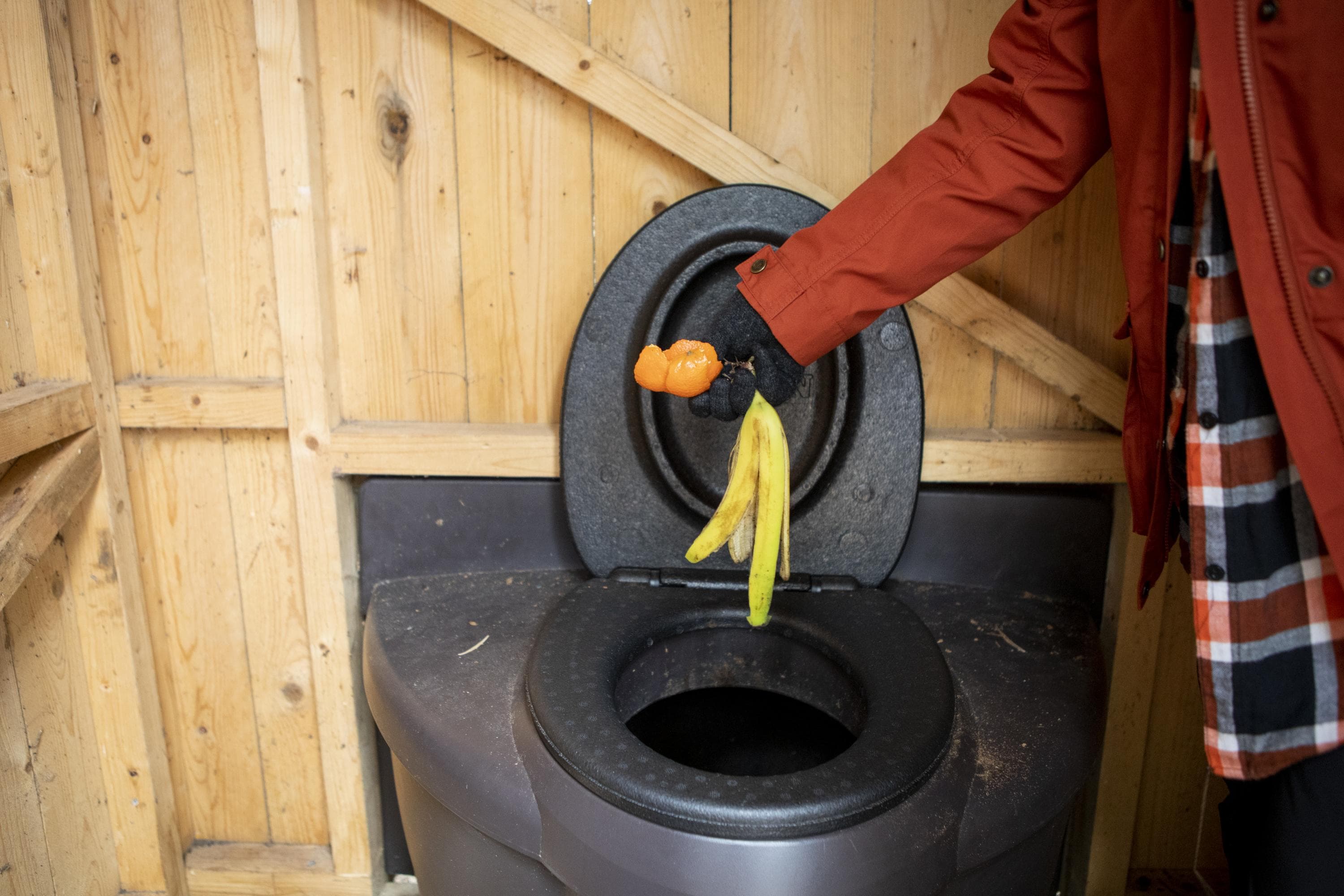 Kuva: Saara Tuominen Huussin sisältä otetussa kuvassa henkilö on pudottamassa banaanin ja mandariinin kuoria pönttöön.