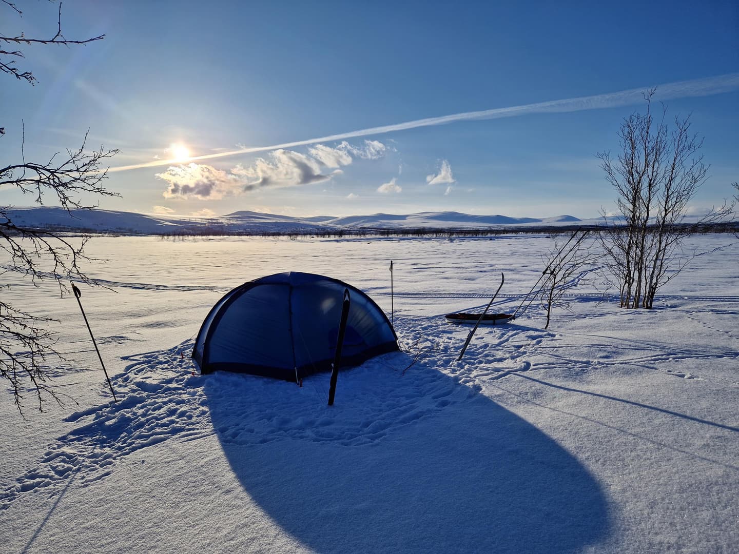 Bild: Annu Tuohiluoto Ett tält uppsatt på snön, med en pulka bredvid. Fjäll i bakgrunden bortom den öppna ytan.