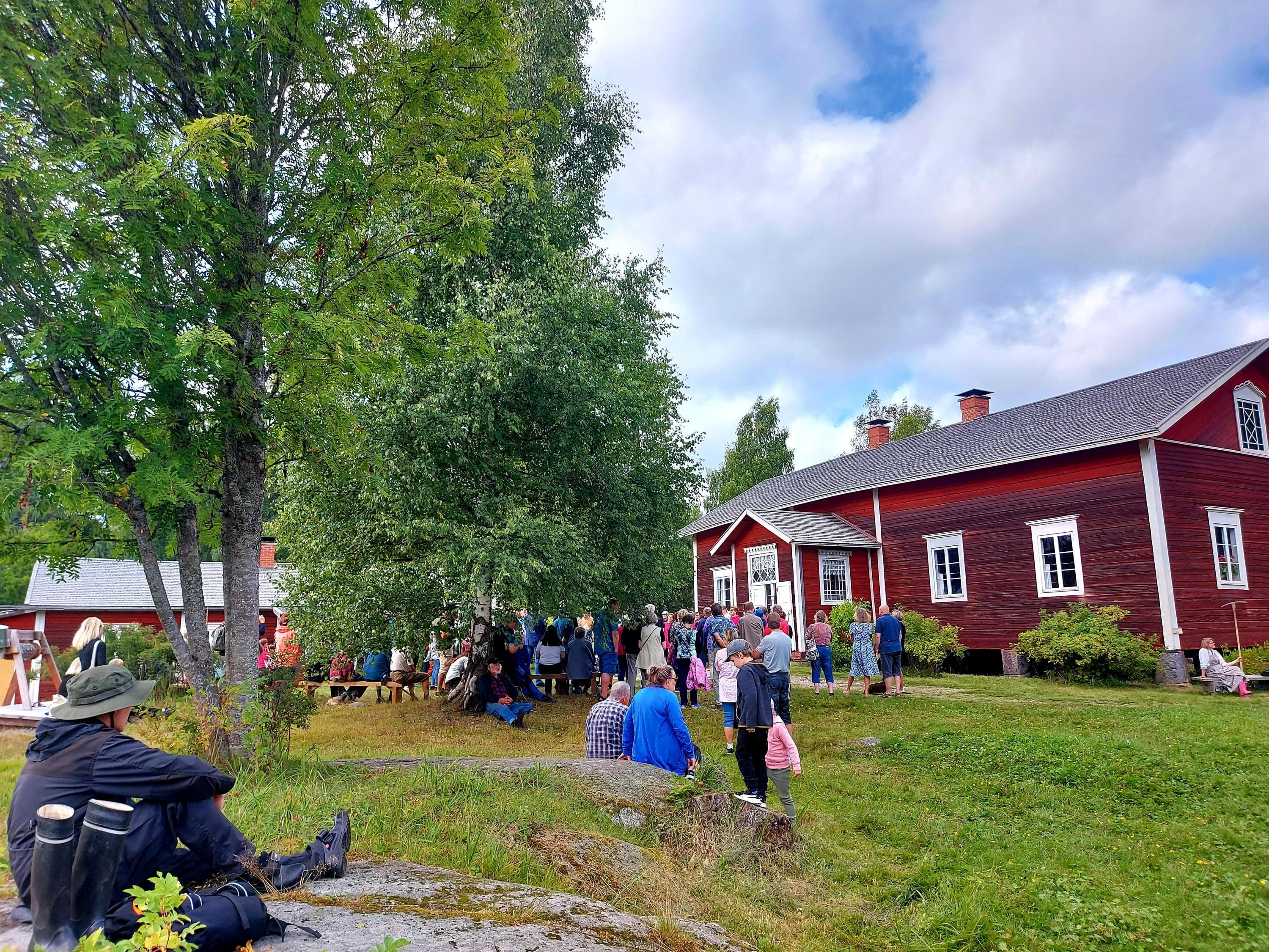 Kuva: Teemu Rintala Punainen, vanha hirsirakennus, jonka pihalla on paljon ihmisiä.