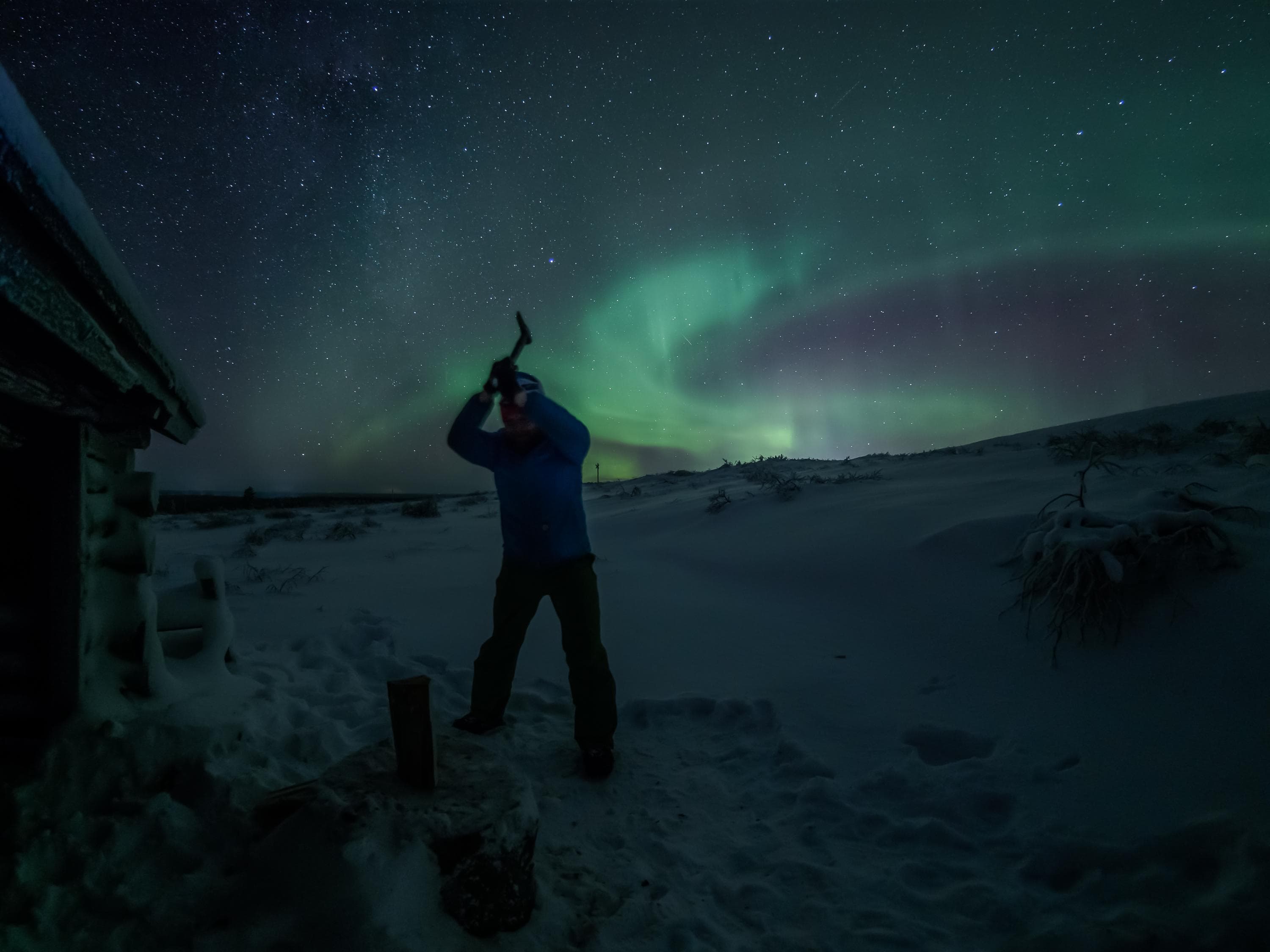 Image: Sampsa Sulonen The hiker chops firewood in winter. The northern lights blaze in the sky.