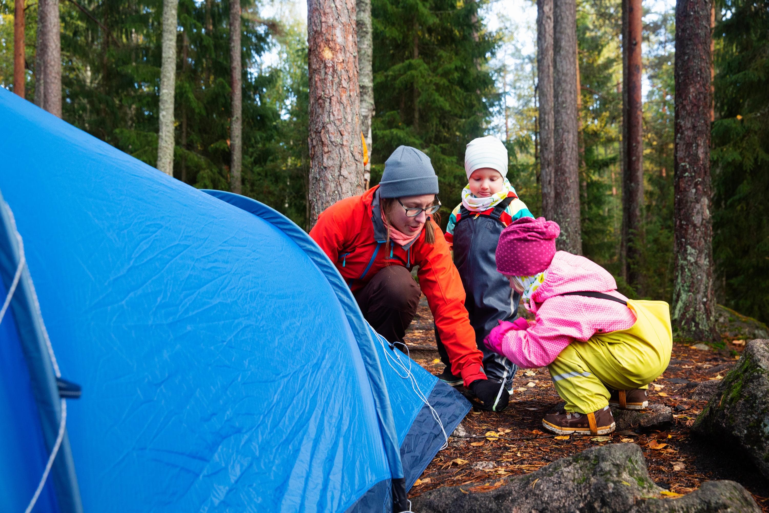 Kuva: Katri Lehtola Aikuinen ja lapset pystyttävät telttaa syksyllä metsässä.