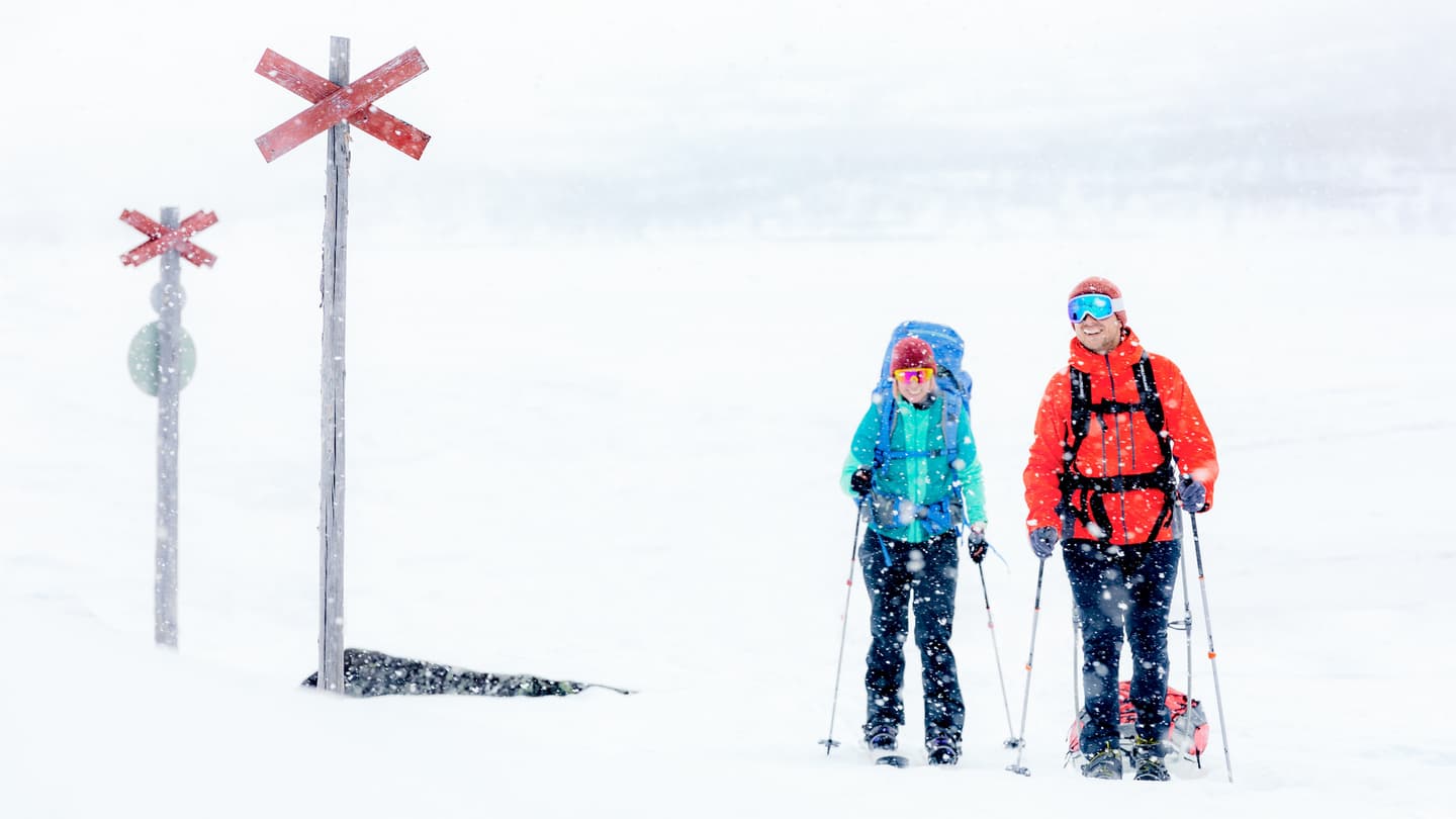 Image: Rami Valonen Two skiers in a snowfall. Behind the skiers, there are two snowmobile track markers.