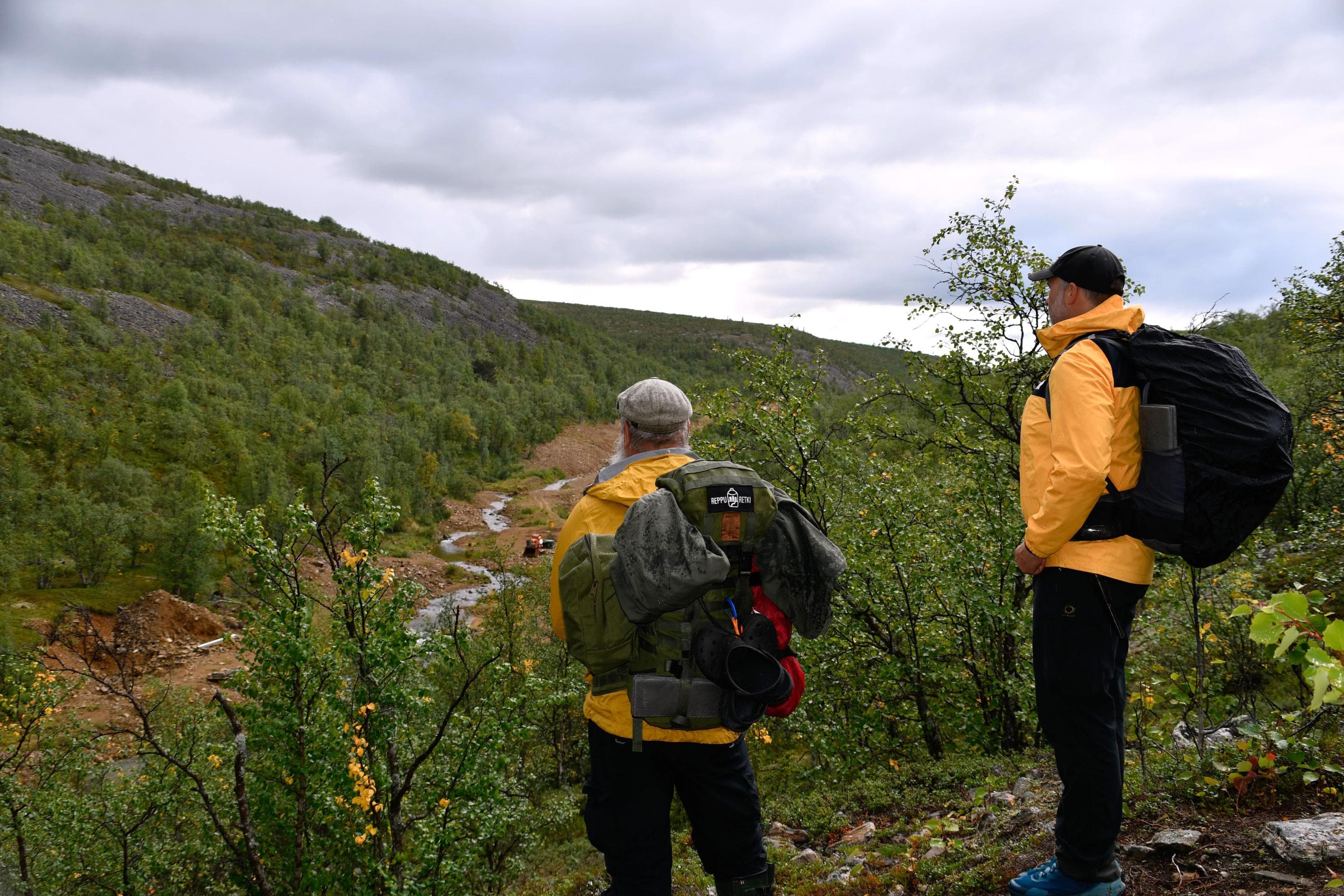 Kuva: Kirsi Ukkonen Kaksi henkilöä seisoo rinteellä ja katsoo alas laaksoon, jossa on puro.
