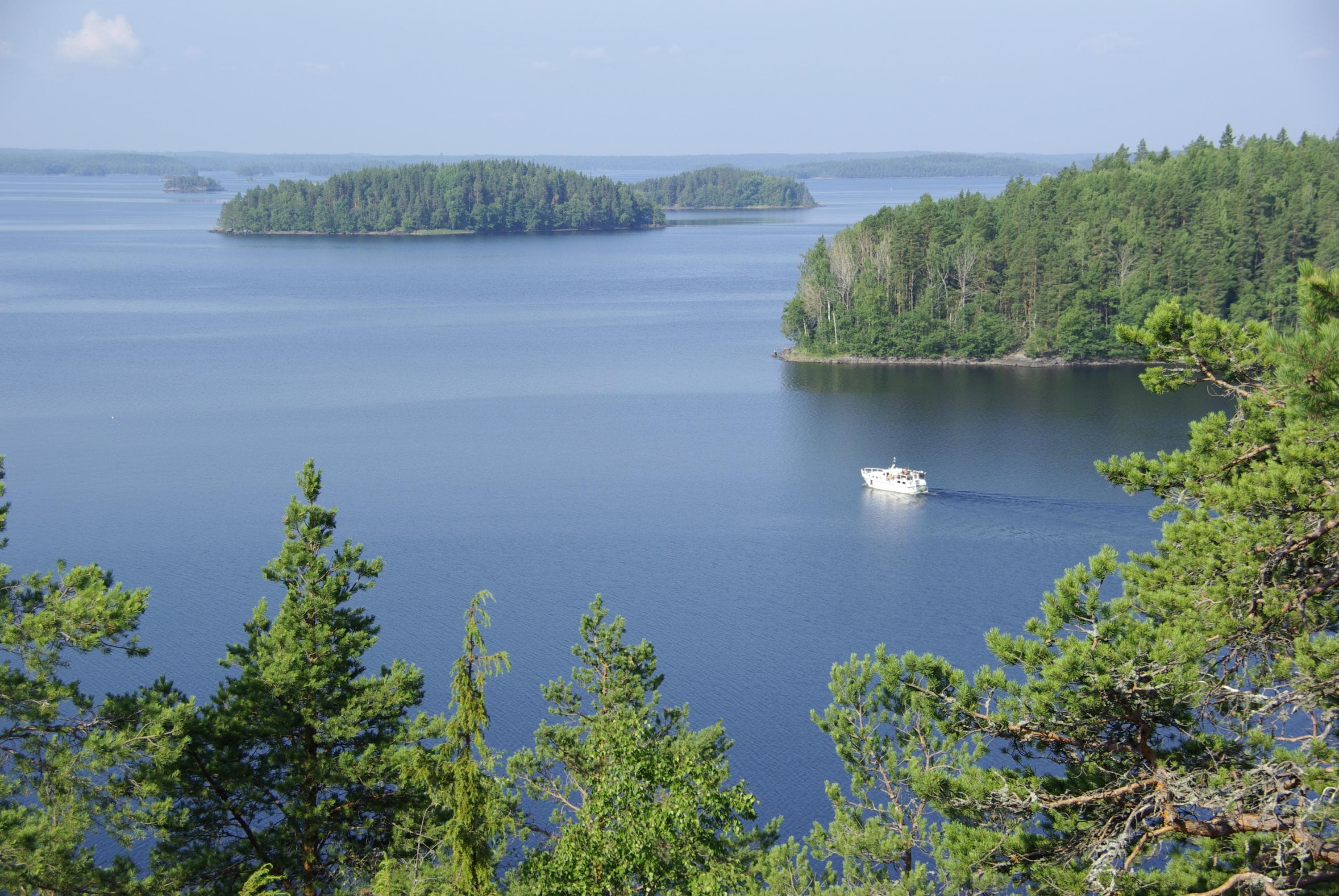 Image: Anne Pyykönen Kesäinen järvimaisema. Järvellä on vene ja metsäisiä saaria.