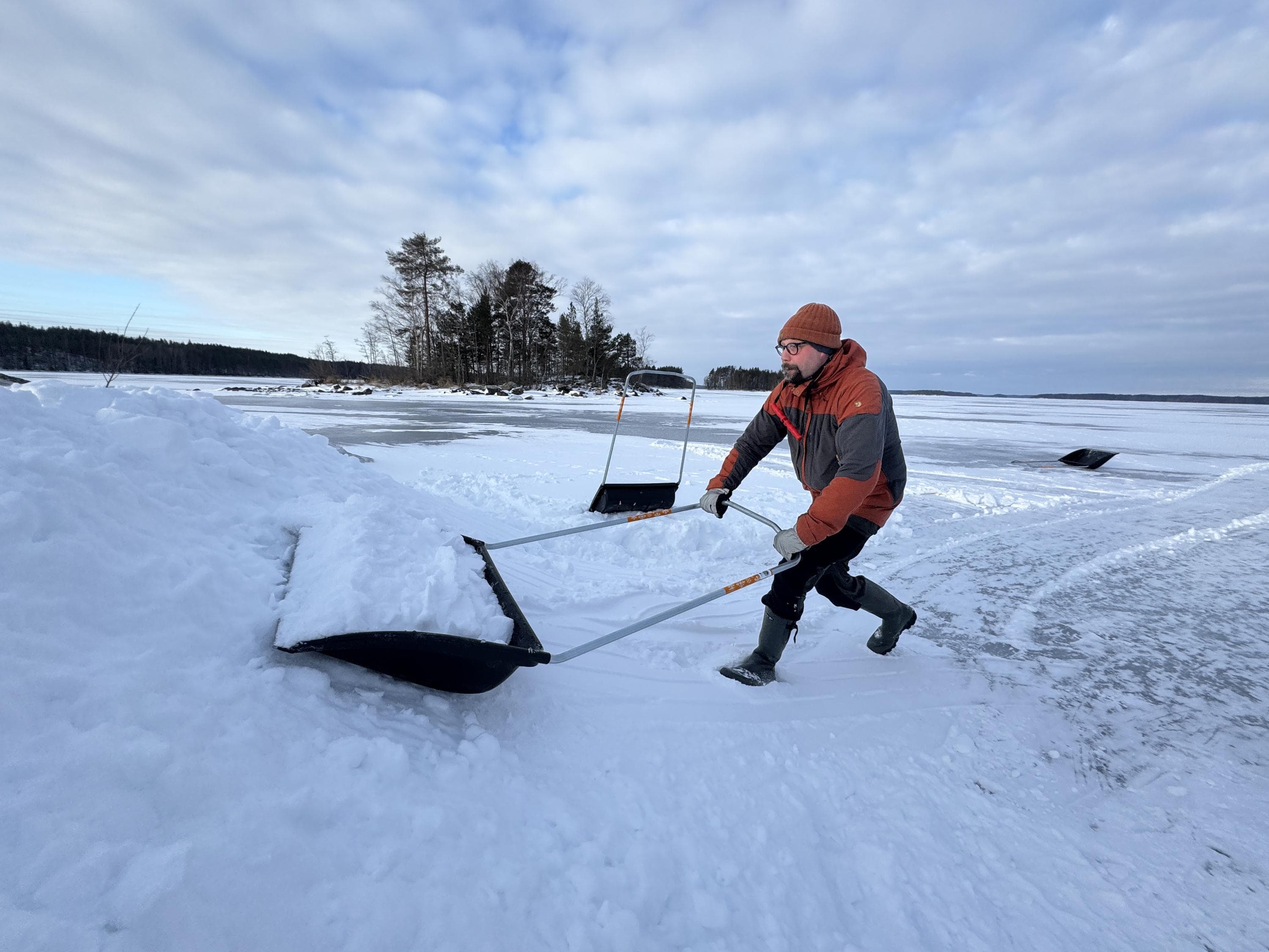 Kuva: Ilkka Numminen. Vapaaehtoinen työntää täynnä lunta olevaa lumikolaa kinoksen päälle.