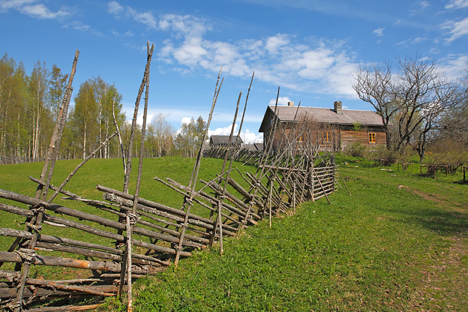 Image: Ismo Pekkarinen An old, weathered house on top of a hill. There is a wooden fence along the cart path.