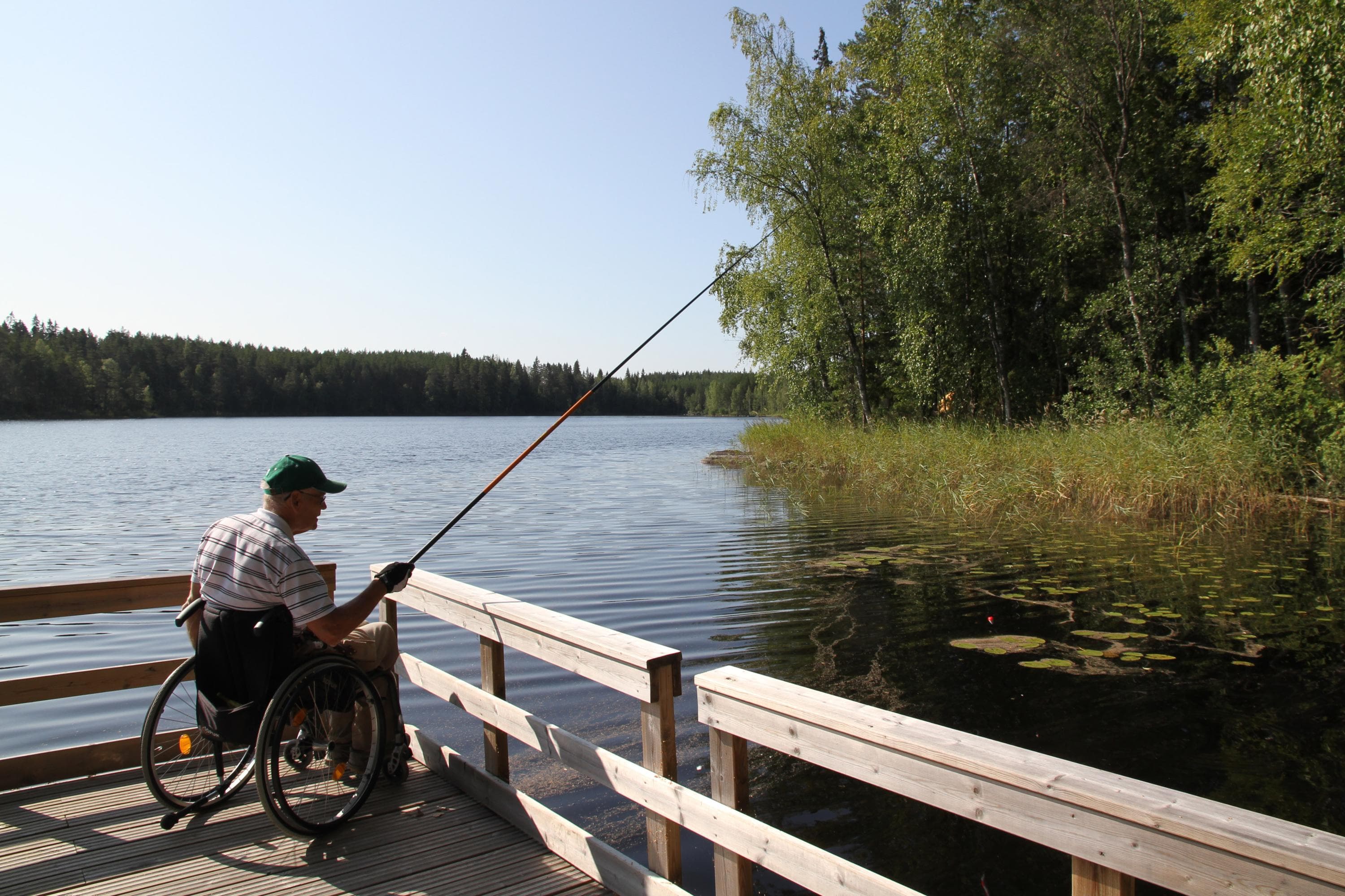Image: Anemone Aaltonen / LUKA A person in a wheelchair fishing from a pier. The pier has wooden railings.