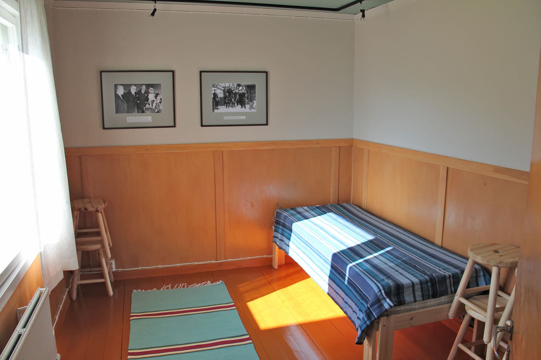 Kuva: Pasi Nivasalo Huoneessa on puolipaneeli ja pari taulua seinällä ja kudottu matto lattialla.