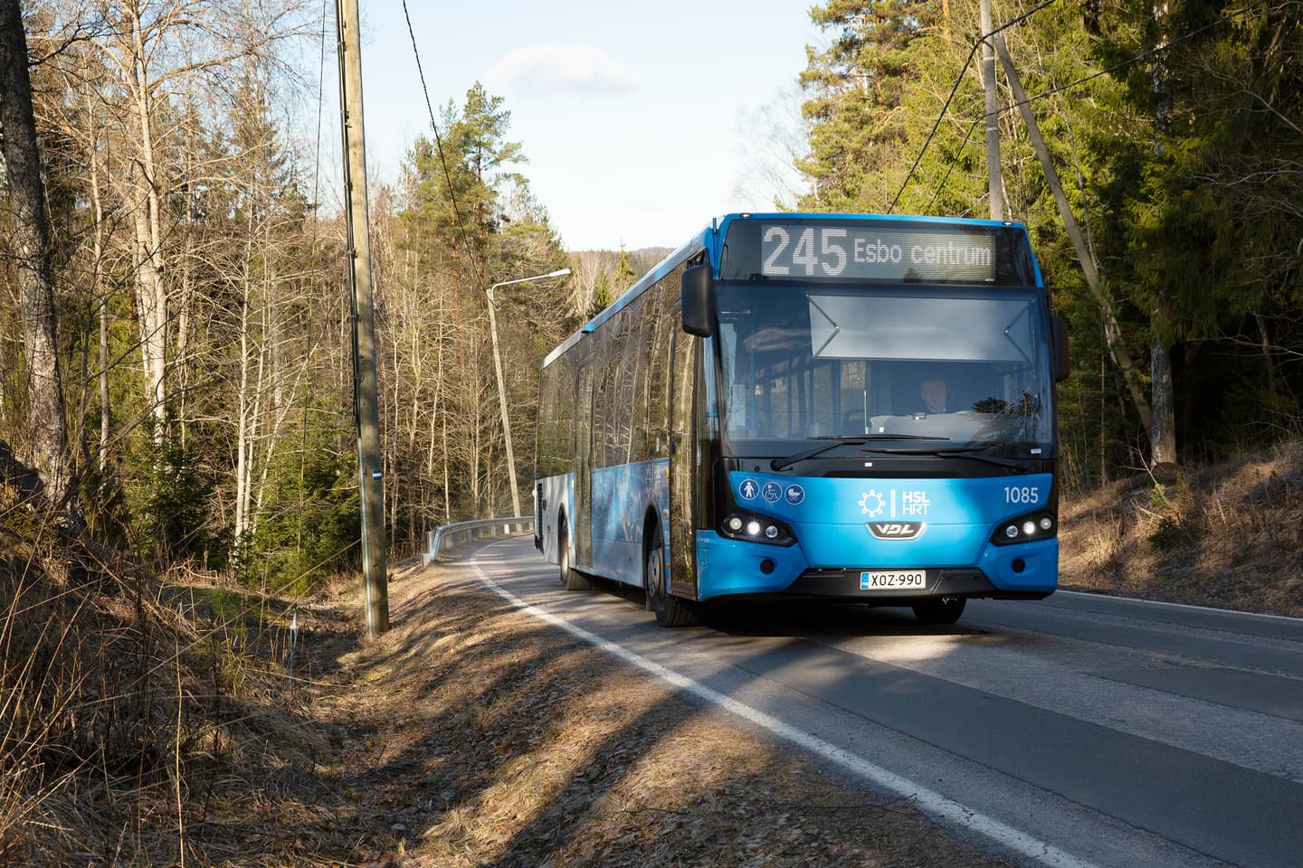 Image: Katri Lehtola Bus 245 to Espoo Centre drives uphill on an asphalt road surrounded by forest.
