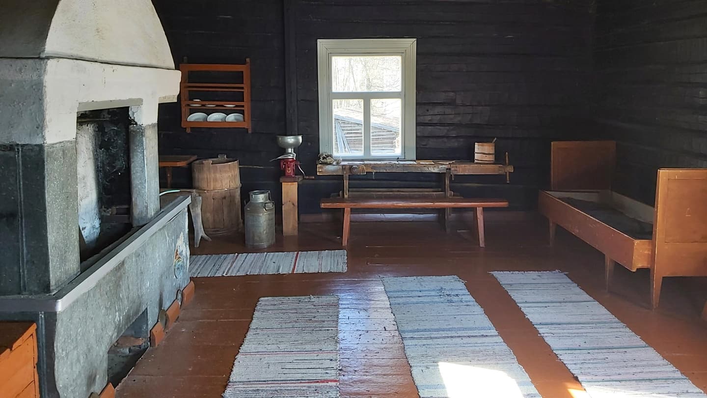 Image: Tiina Linsén The interior of an old croft. Long rag rugs on the floor, a pull-out bed against one wall, a large oven against the other. A window on the back wall.