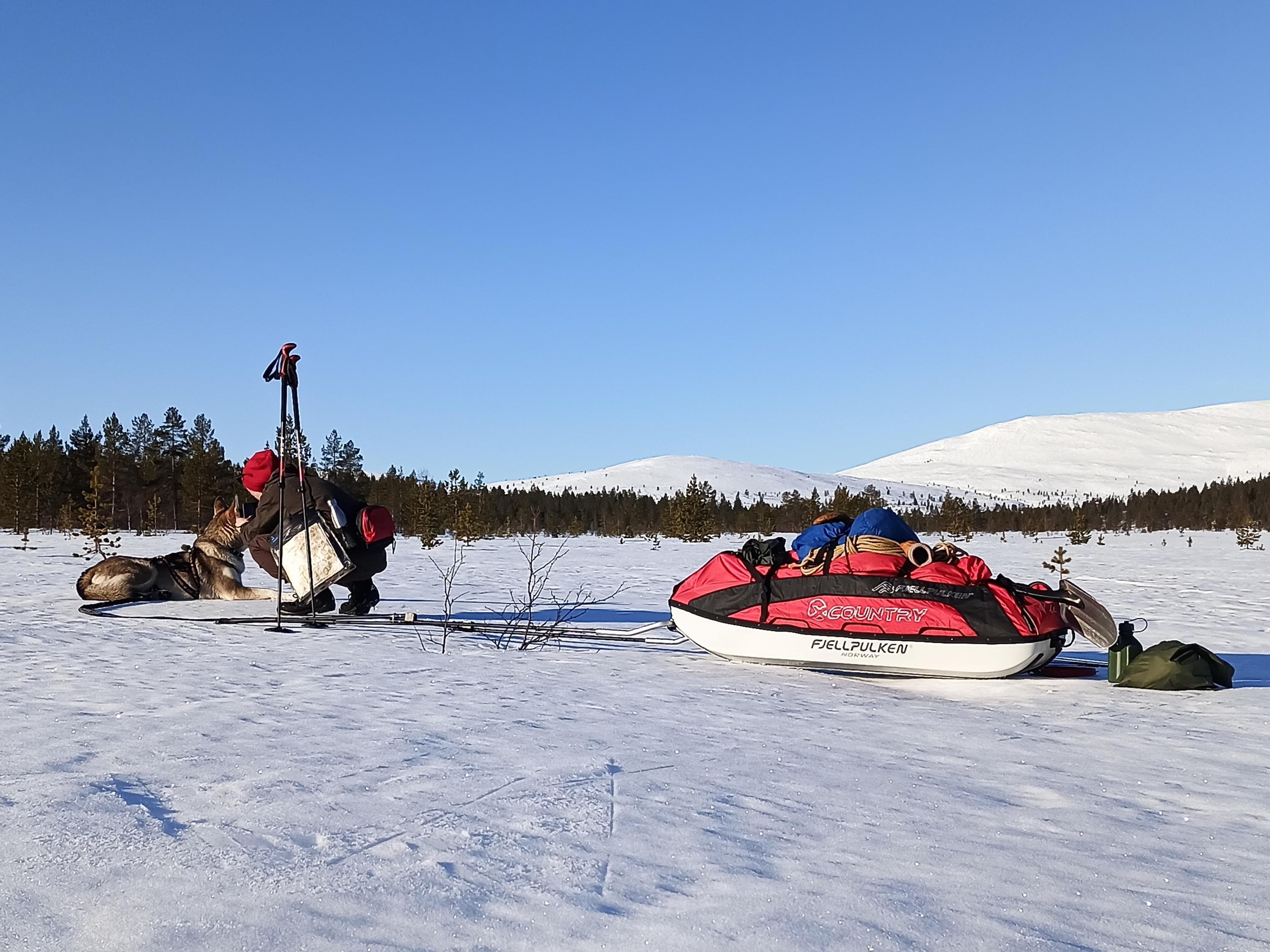Kuva: Leena Leppälä Hiihtäjä rapsuttaa koiraa. Hiihtäjällä on ahkio perässä. Taustalla siintää lumiset tunturit.