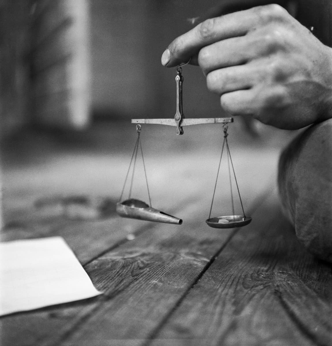 Image: U.A. Saarinen / Museovirasto, Journalistinen kuva-arkisto hand holds a small scale above a wooden table.