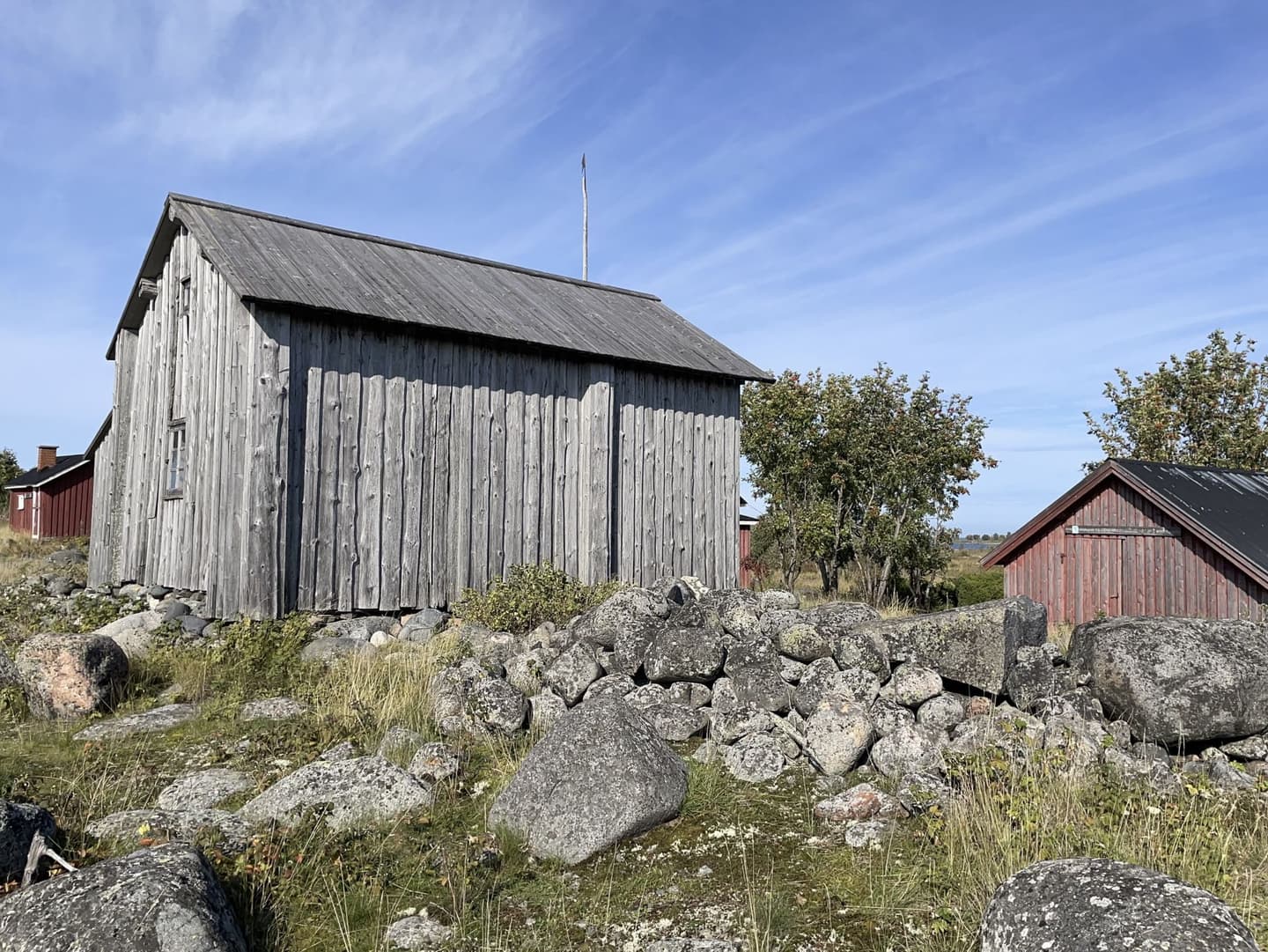 Image: Päivi Tervonen An old grey wooden building in the middle of a rocky area. To the right of the building, there is a smaller red wooden building.
