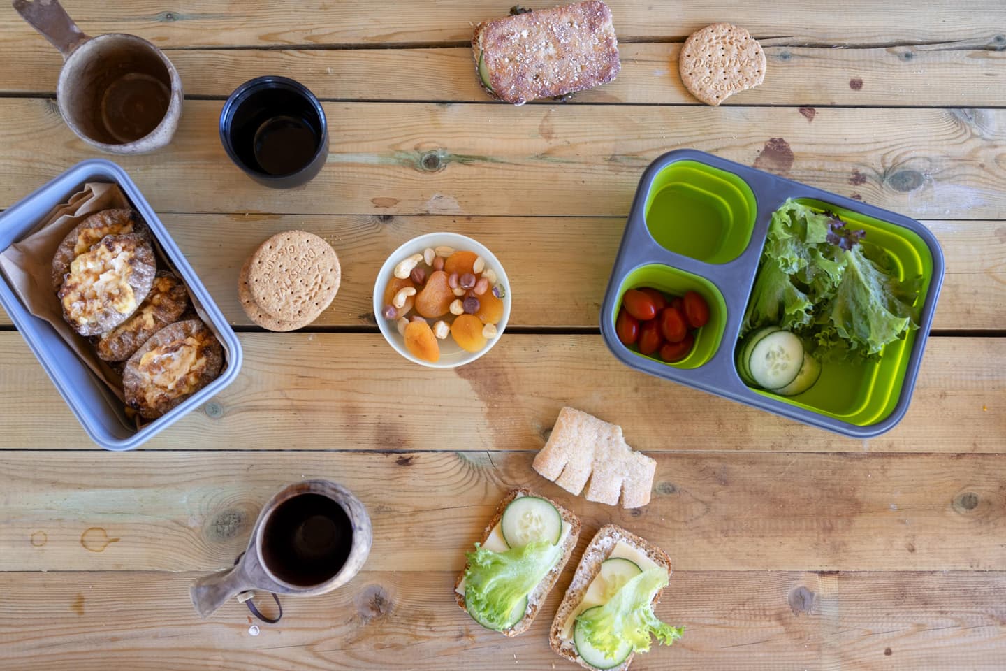 Image: Harri Tarvainen On a wooden table there are sandwiches, sweet pastries, lunch boxes and wooden cups filled with coffee.