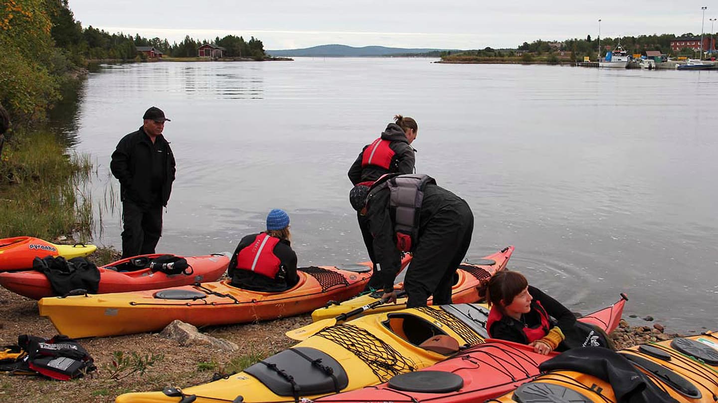Image: Riina Tervo Kayaks on the shore, being packed by paddlers. The weather is cloudy.