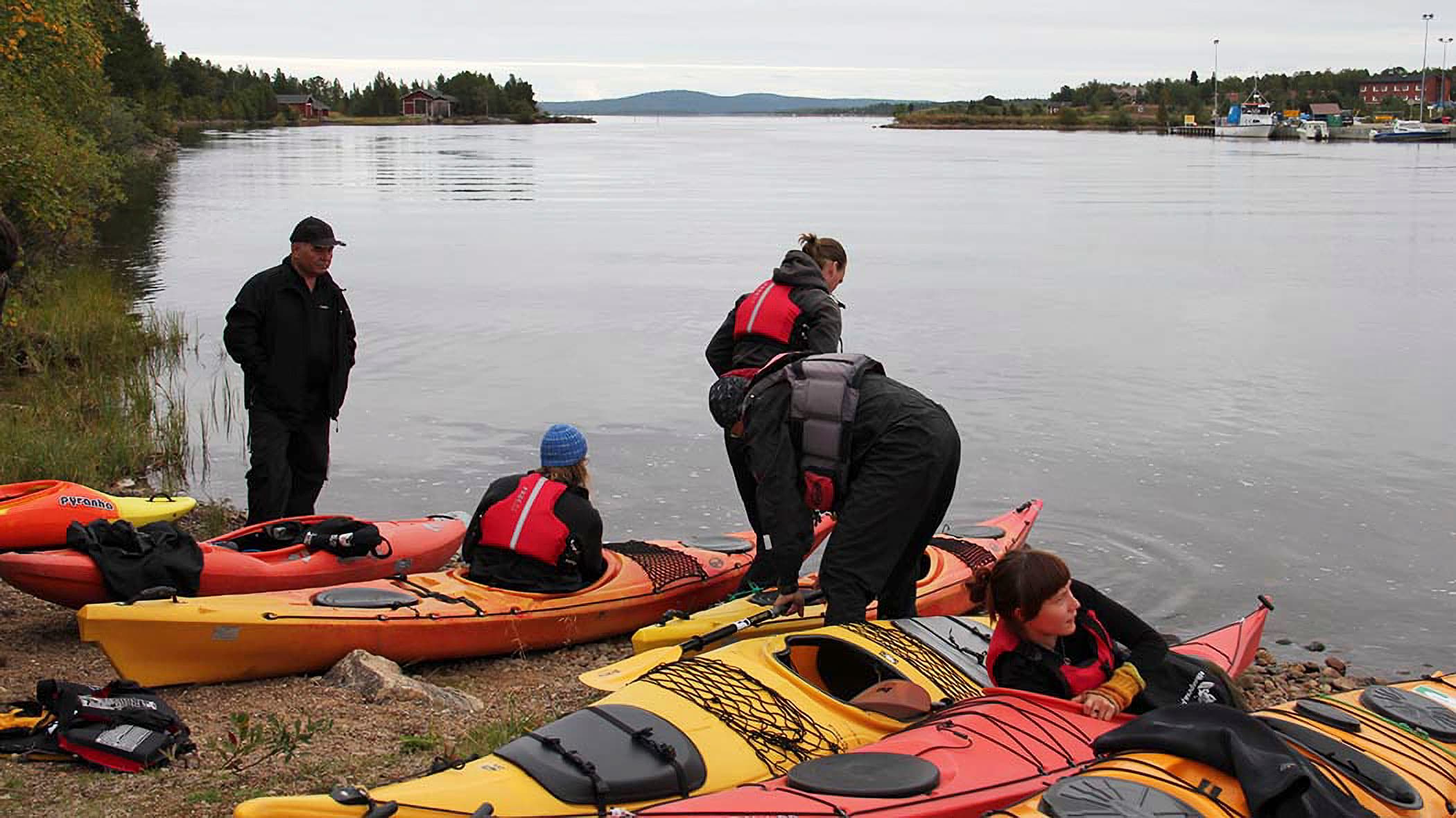 Image: Riina Tervo Kayaks on the shore, being packed by paddlers. The weather is cloudy.