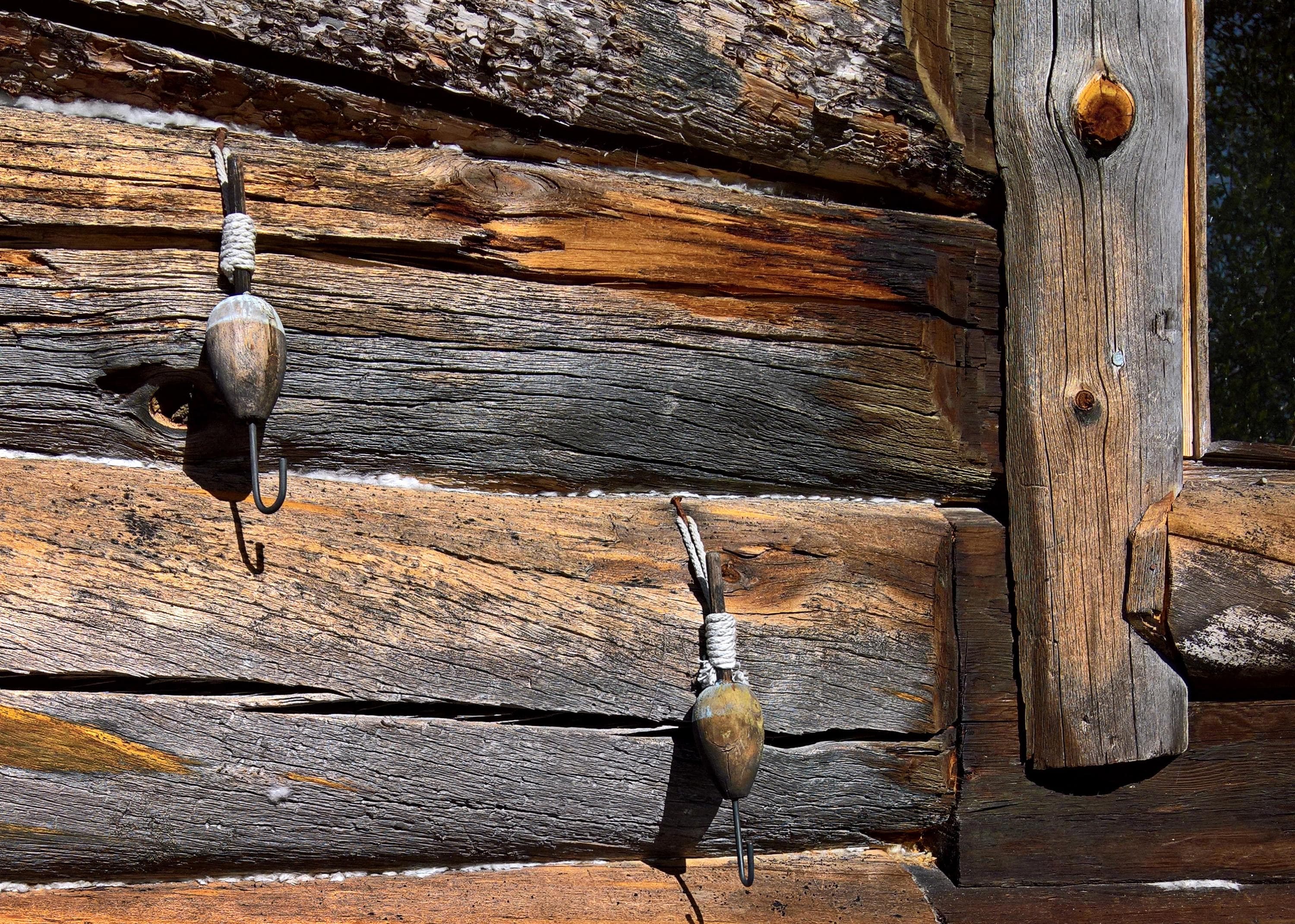 Image: Anna Pakkanen A grayed log wall with two old fishing hooks attached to it.