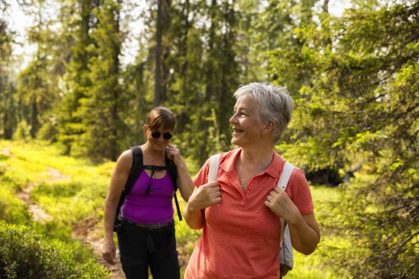 Image: Harri Tarvainen In the foreground of the image, there are two smiling women. In the background, there is a forest, and the day is sunny.