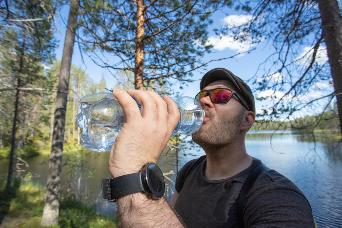 Image: Minna Niinistö A hiker drinks clear water from a water bottle in the forest. A lake is visible in the background.