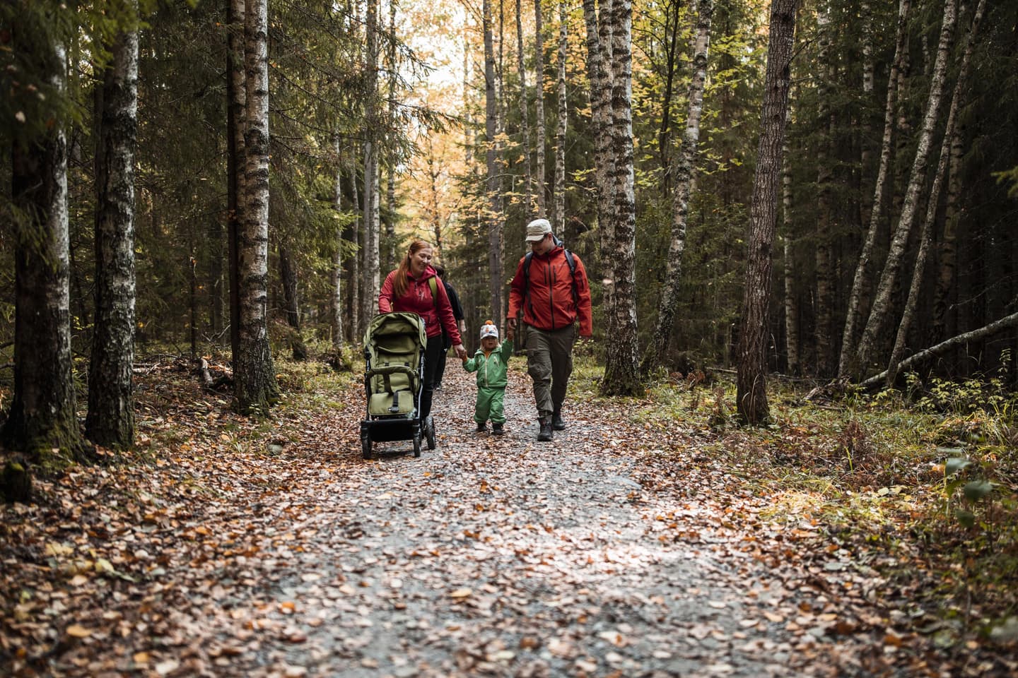 Image: Maarit Vaahteranoksa A family with a buggy is walking along a wide path covered with hard rock dust in an autumnal forest.