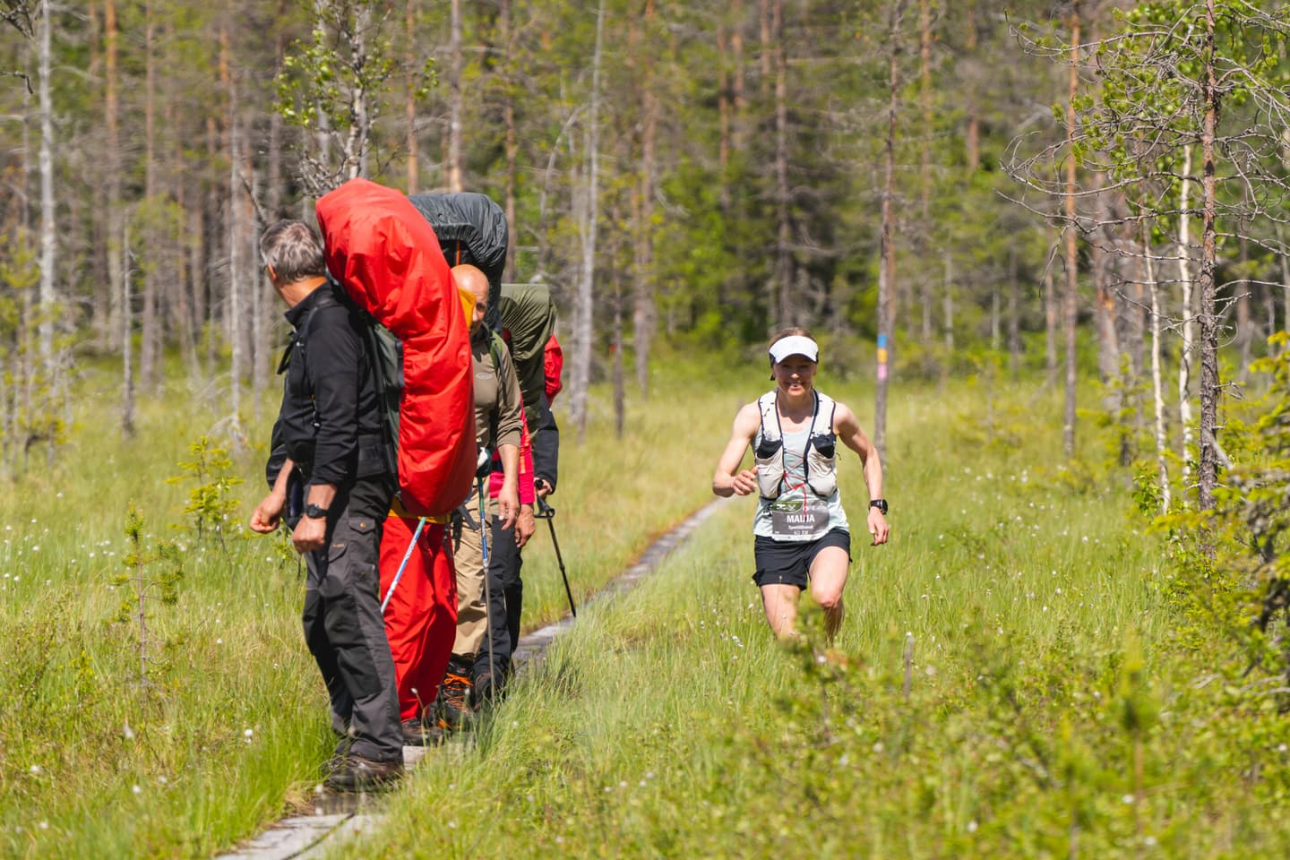 Image: Rami Valonen Retkeilijöitä pitkospuilla rinkat selässä, joita juoksija ohittaa suon kautta.