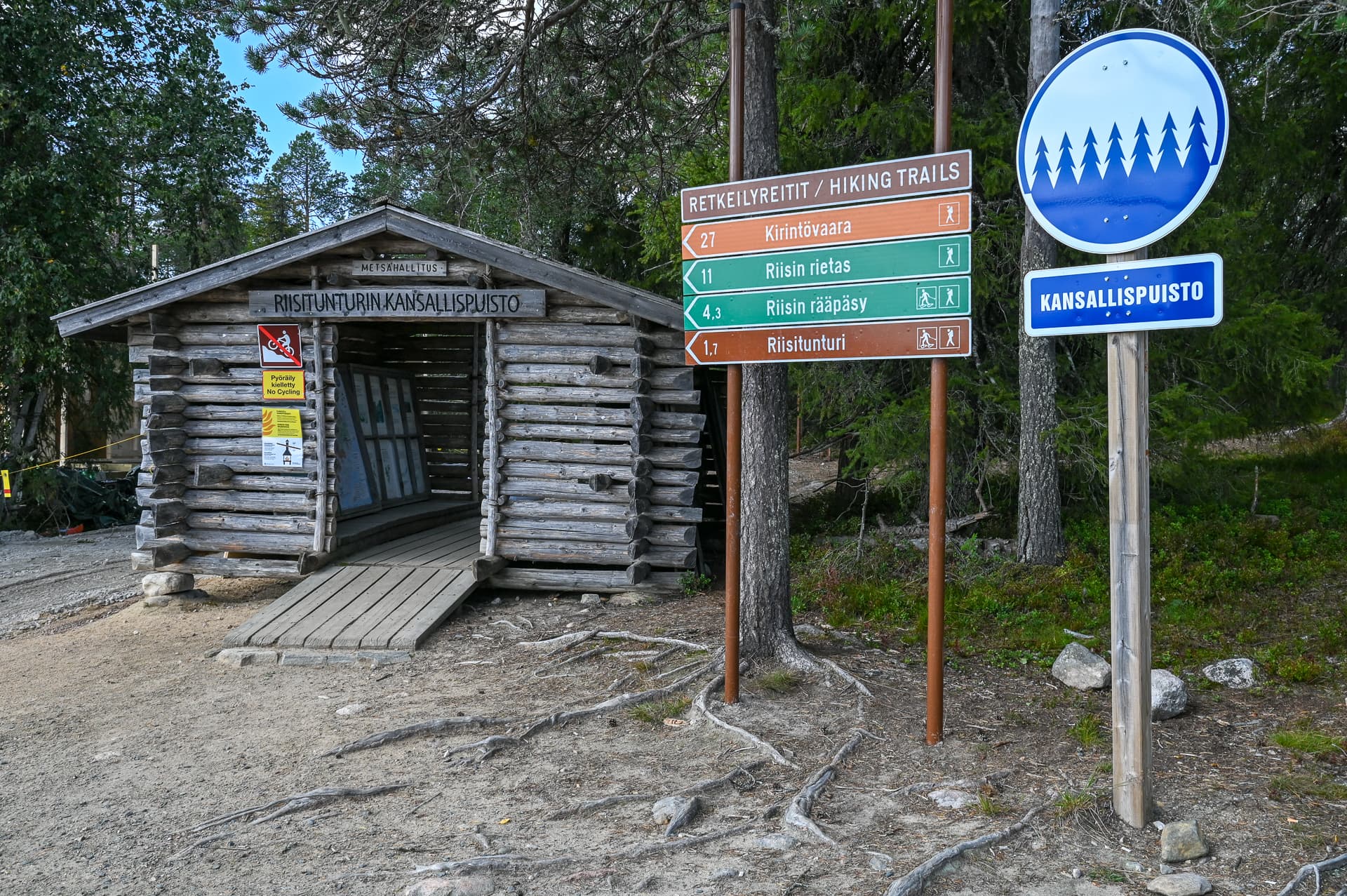 Kuva: Riitta Tiermas Parkkipaikan reunalla on opastuskatos, reittiviittoja ja kansallispuiston merkki.