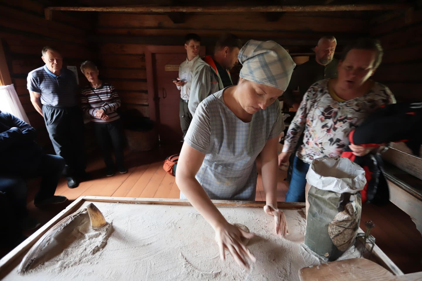 Image: Jari Salonen A woman is baking traditional rye hole bread in the cottage. People are observing the baking process.