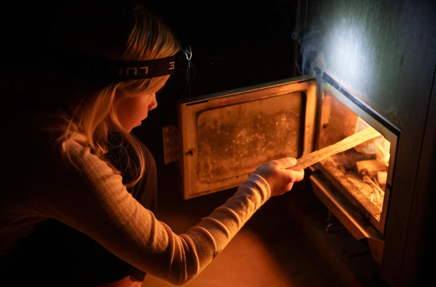 Image: Katri Lehtola A person is feeding logs into the stove's firebox, where the fire is burning.