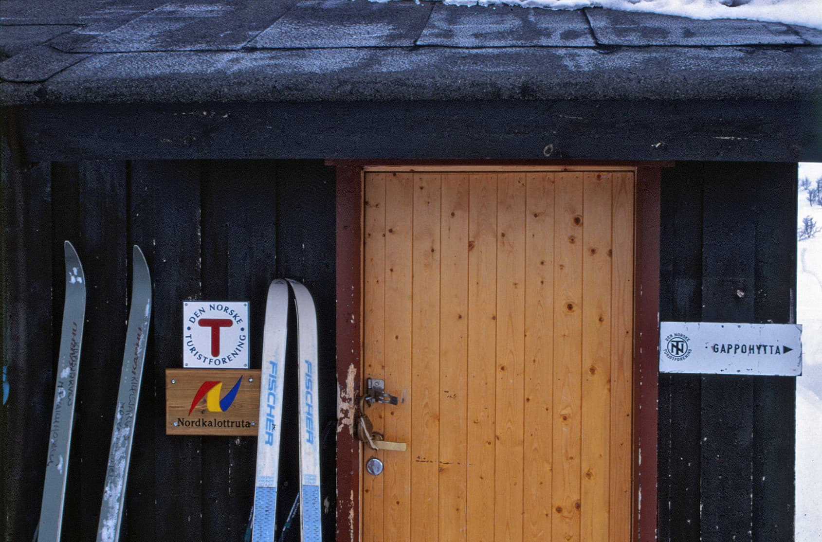 Kuva: Tage Lampen Norjalaisen itsepalvelutuvan ovi, jonka vieressä kahdet sukset seinää vasten.