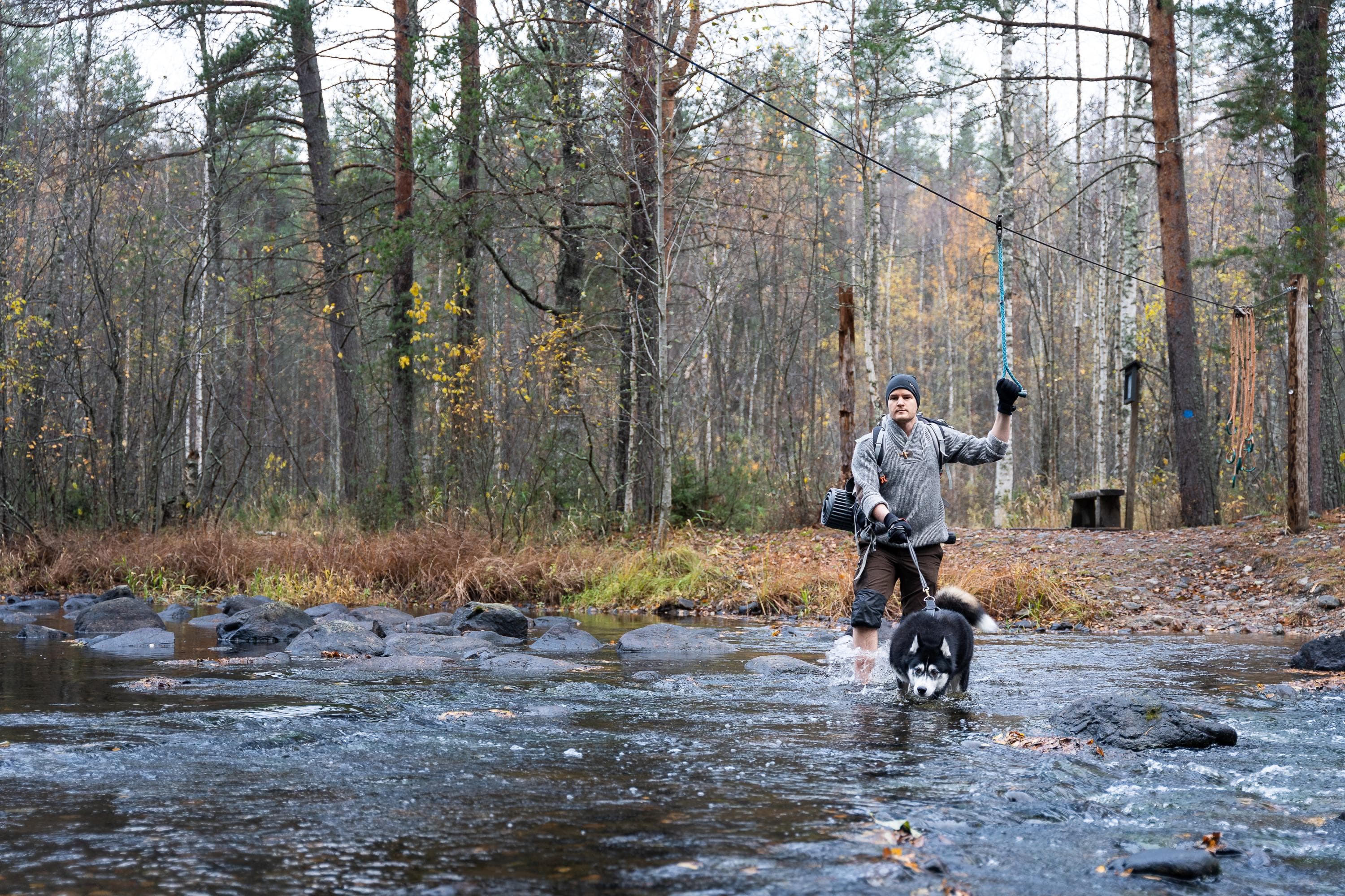 Bild: Mitja Piipponen En vandrare och en hund vadar över en grund flod.