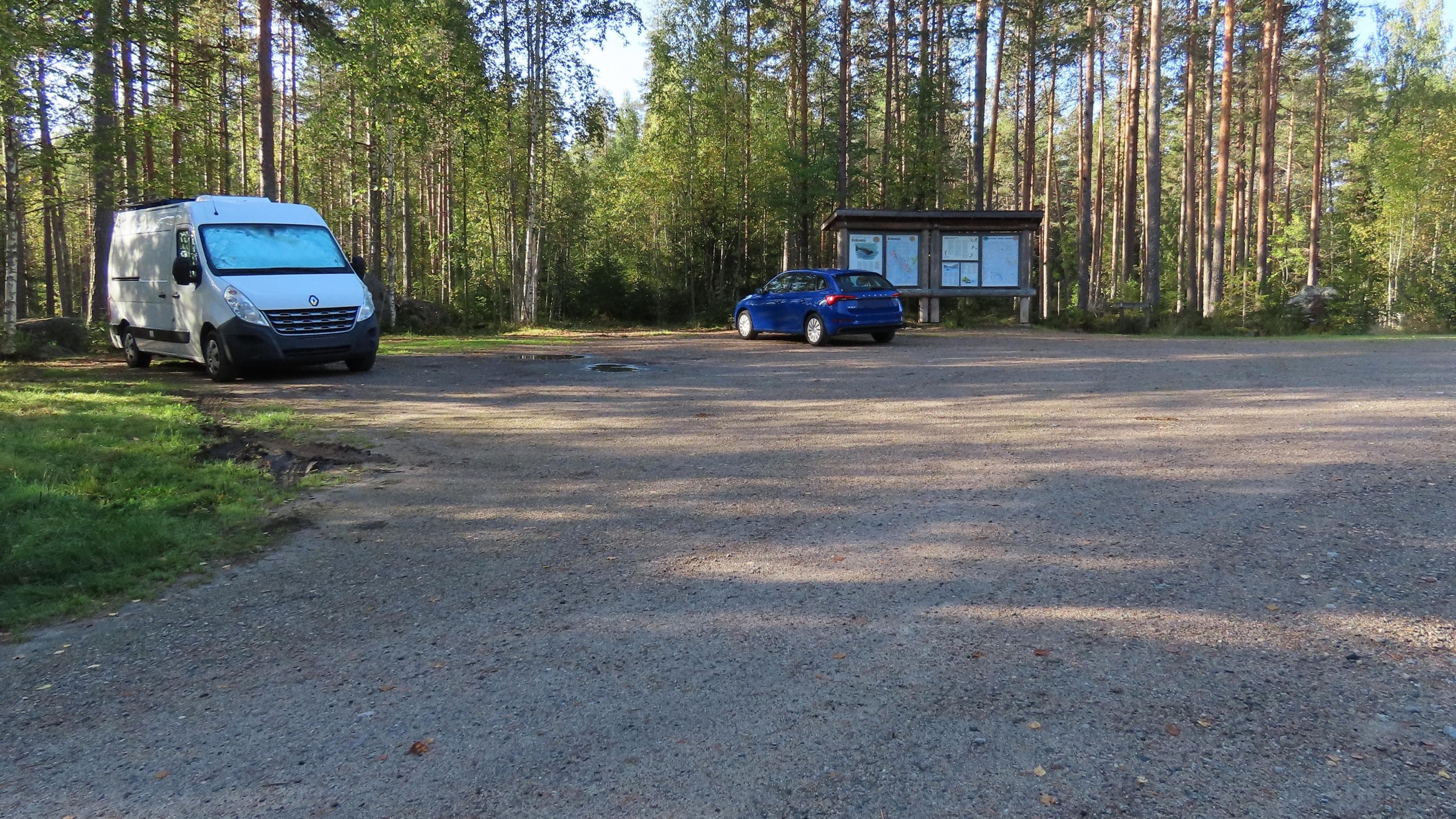 Image: Tiina Linsén Kaksi autoa ja opastetaulu metsässä olevalla pysäköintialueella.