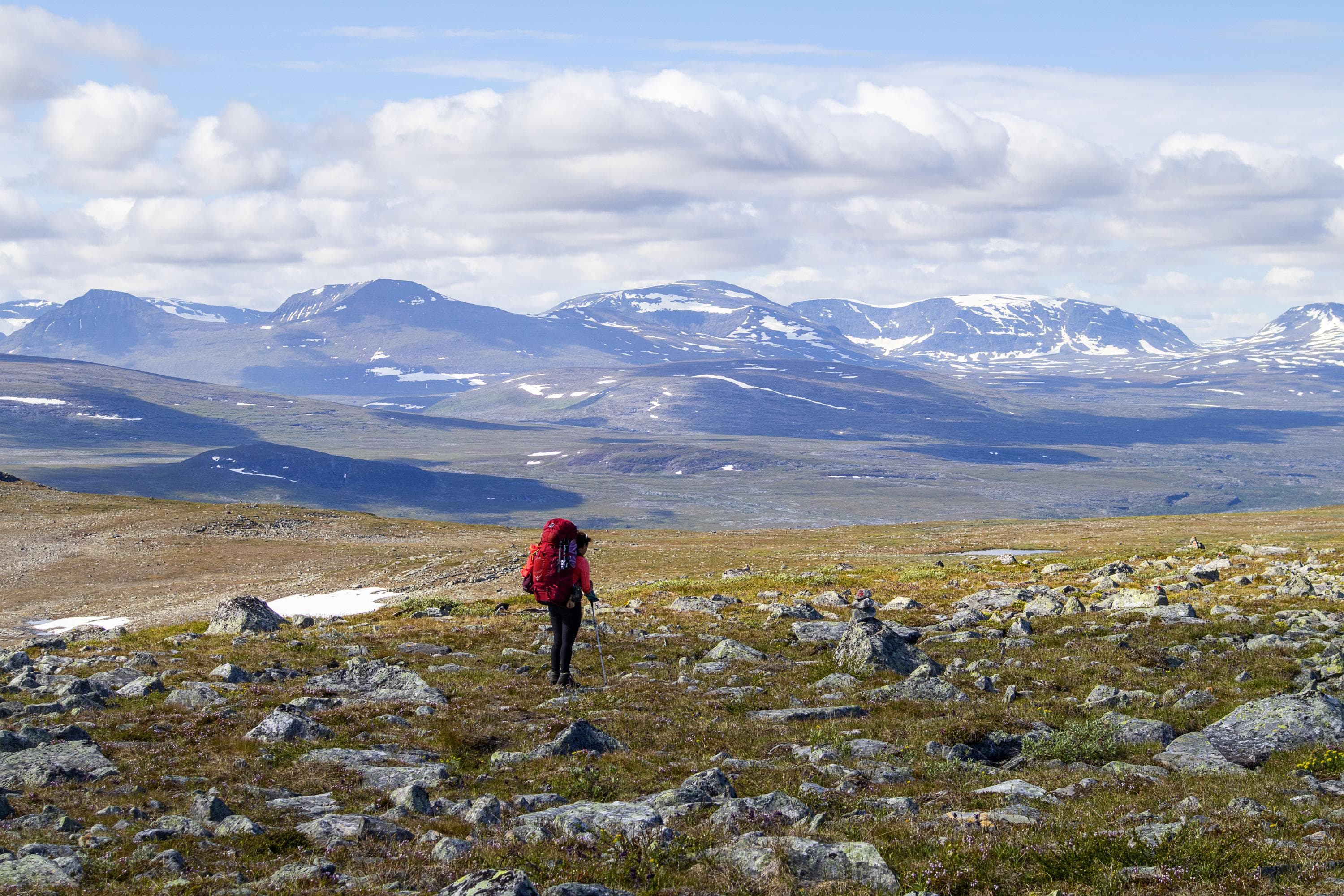 Kuva: Anna Pakkanen Vaeltaja rinkka selässään kivikkoisessa maastossa taustalla kauempana tunturit. Lumilaikkuja näkyvissä siellä täällä.