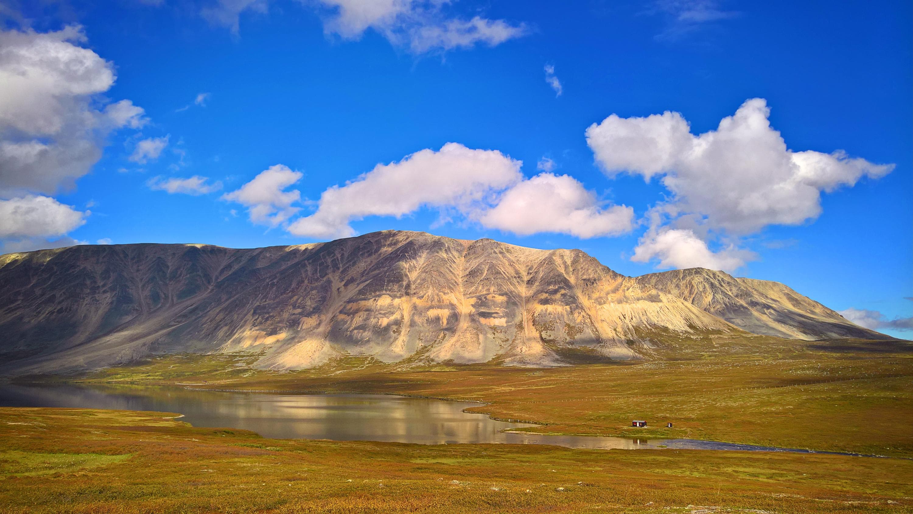 Kuva: Anna Pakkanen Kaksi pientä rakennusta veden äärellä. Kauempana taustalla tunturirinteet.