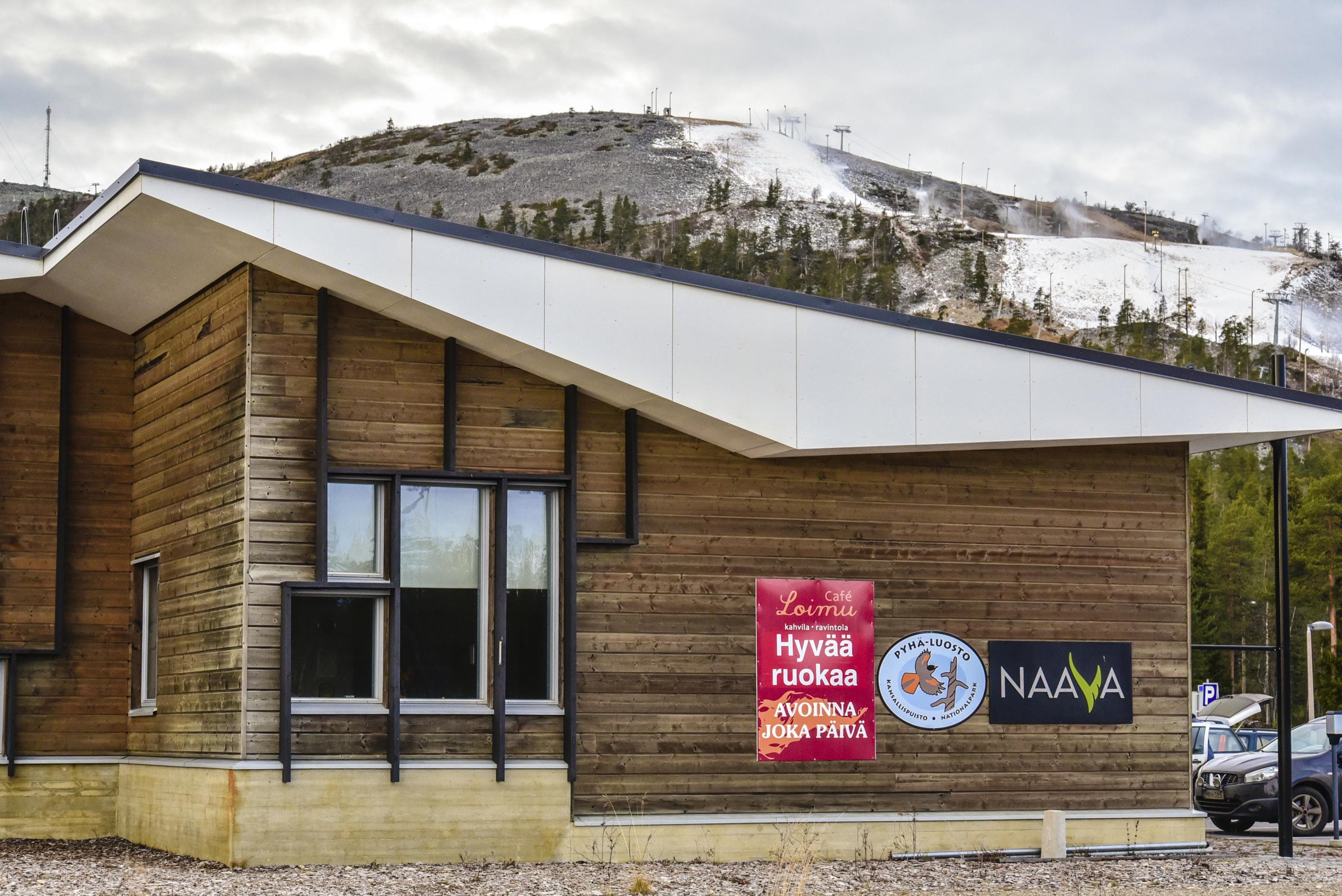 Hirsisen rakennuksen seinällä kylttejä, joista yhdessä lukee NAAVA. Rakennuksen taustalla tunturi.