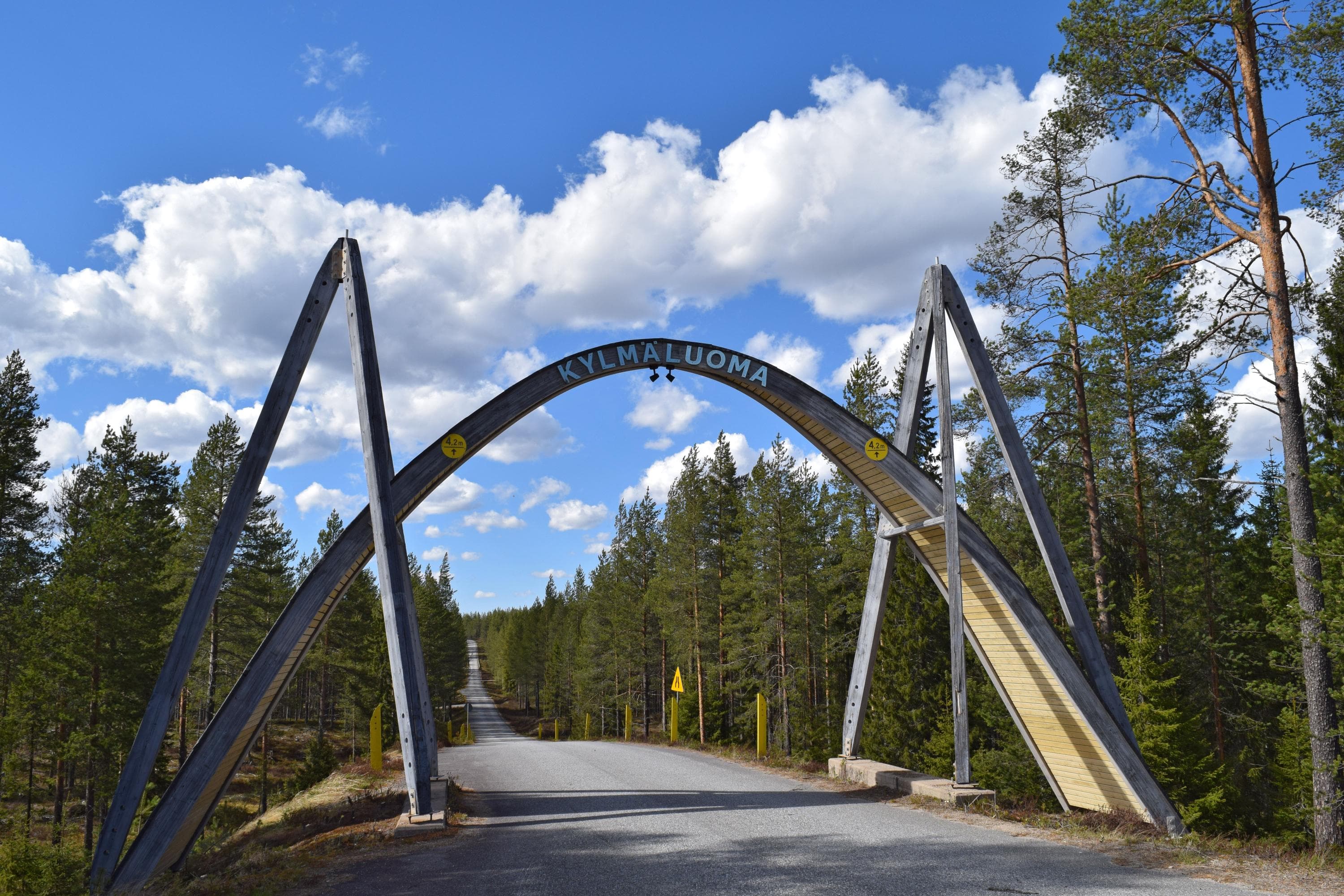 Kuva: Sirke Seppänen Tien reunoilla ja yllä on suuri kaareva puurakennelma, jonka korkeimmalla kohdalla tien päällä lukee Kylmäluoma.