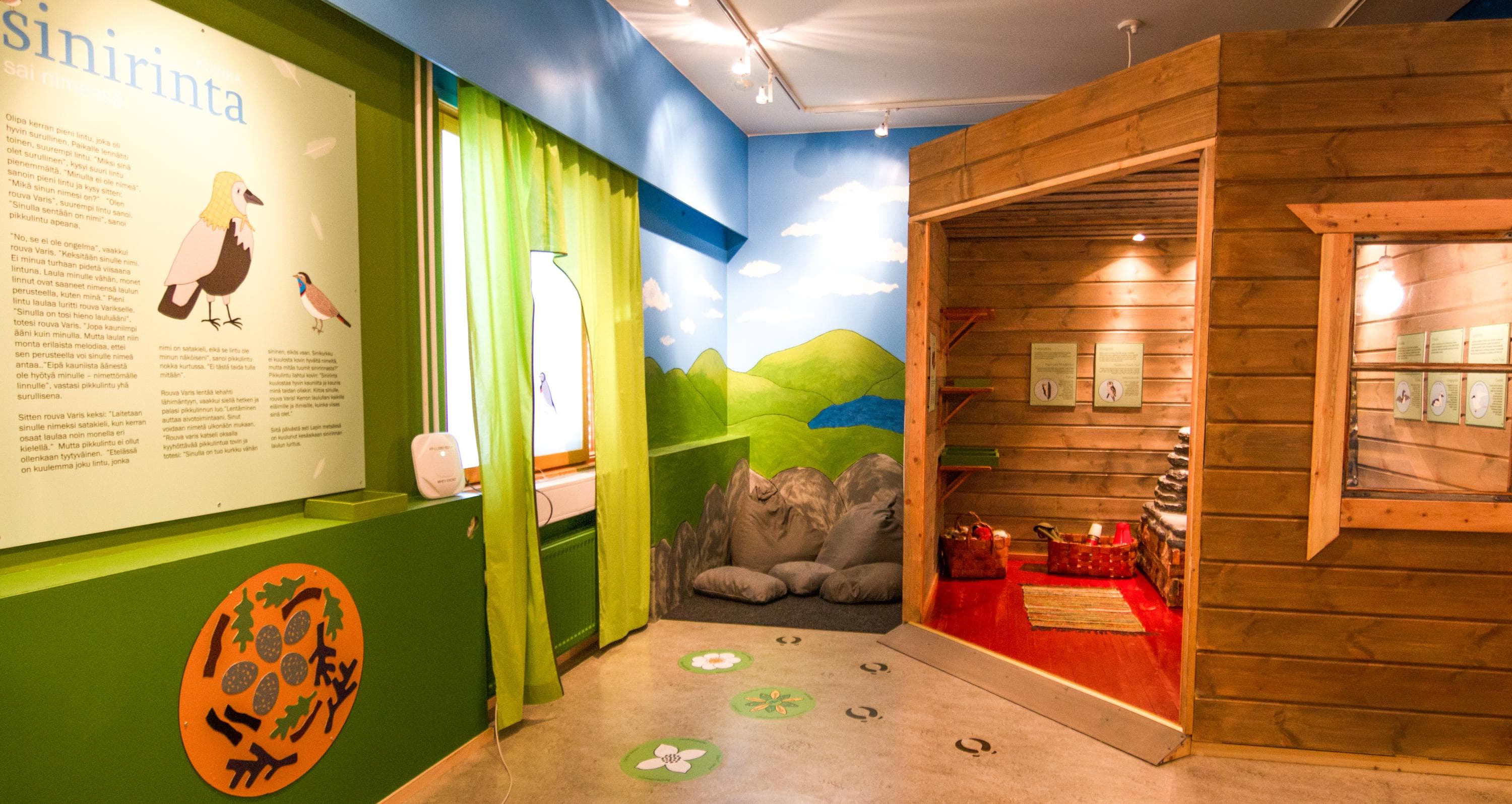 Kuva: Juha Kalaoja Luontokeskuksen lastentila on värikäs. Nurkassa harmaita tyynyjä. Oikealla oikeaa tupaa muistuttava rakenne.