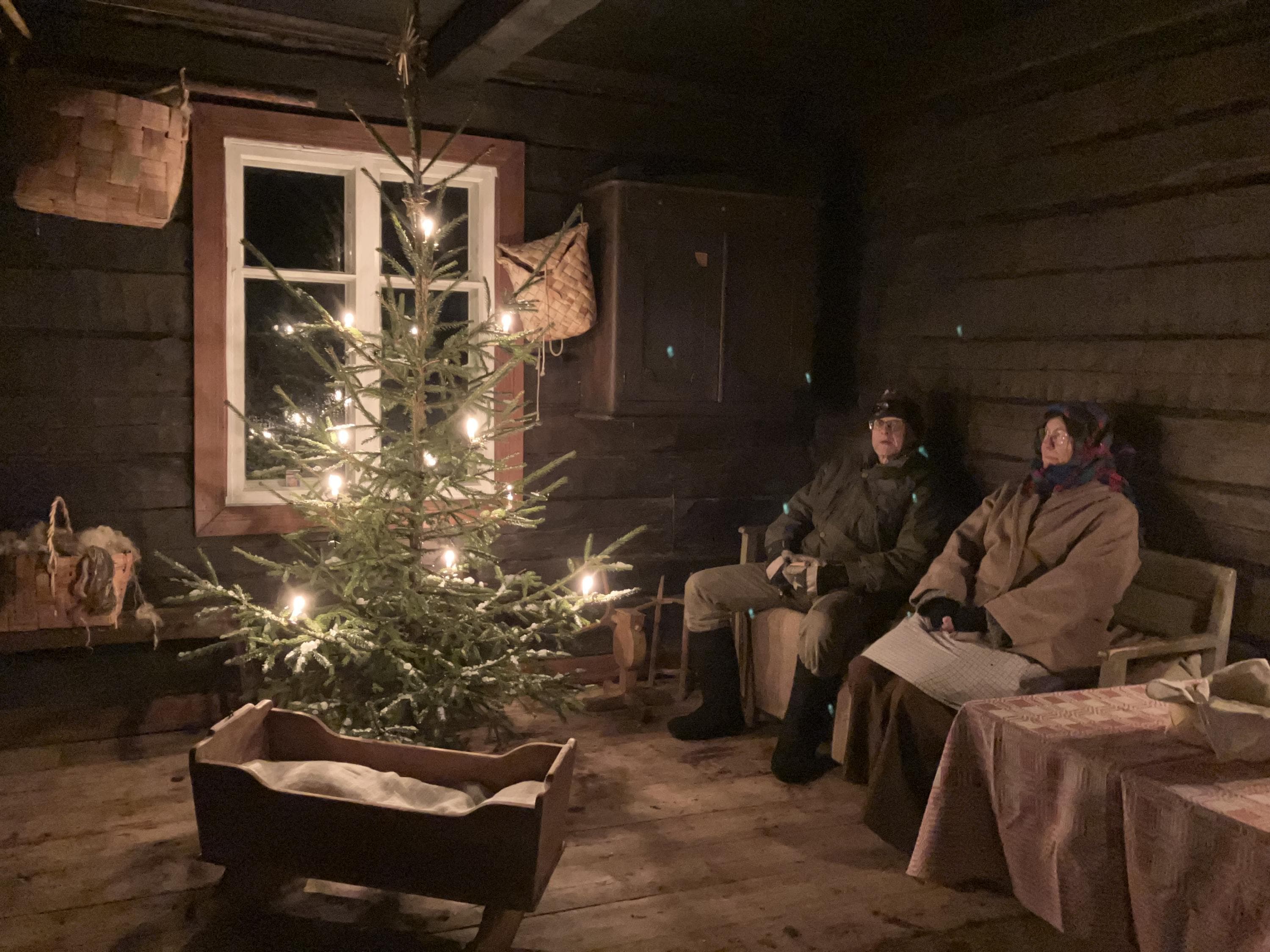 Kuva: Outileena Uotila Henkilöt istuvat vanhassa talossa kuusen ääressä.