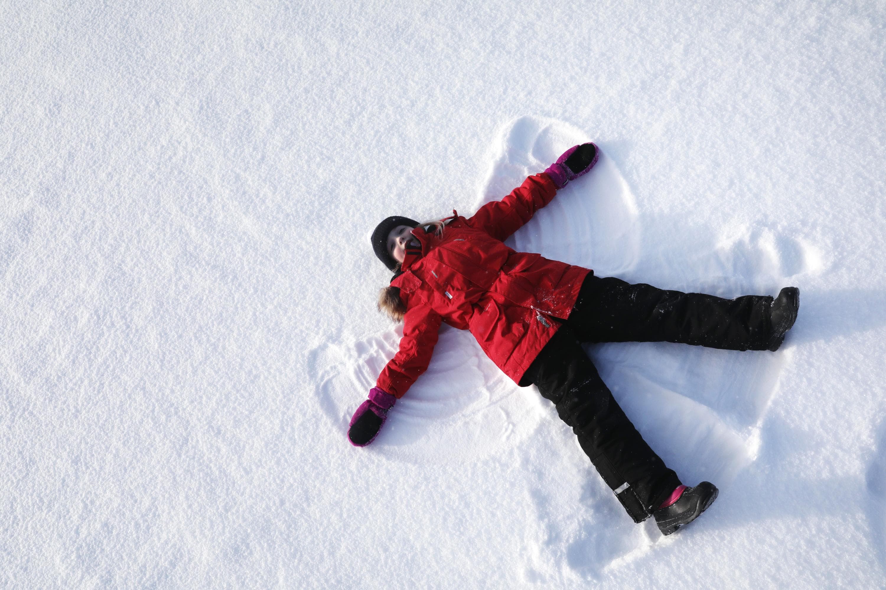 Image: Harri Tarvainen A child dressed in a red winter coat is lying on the snow making a snow angel.