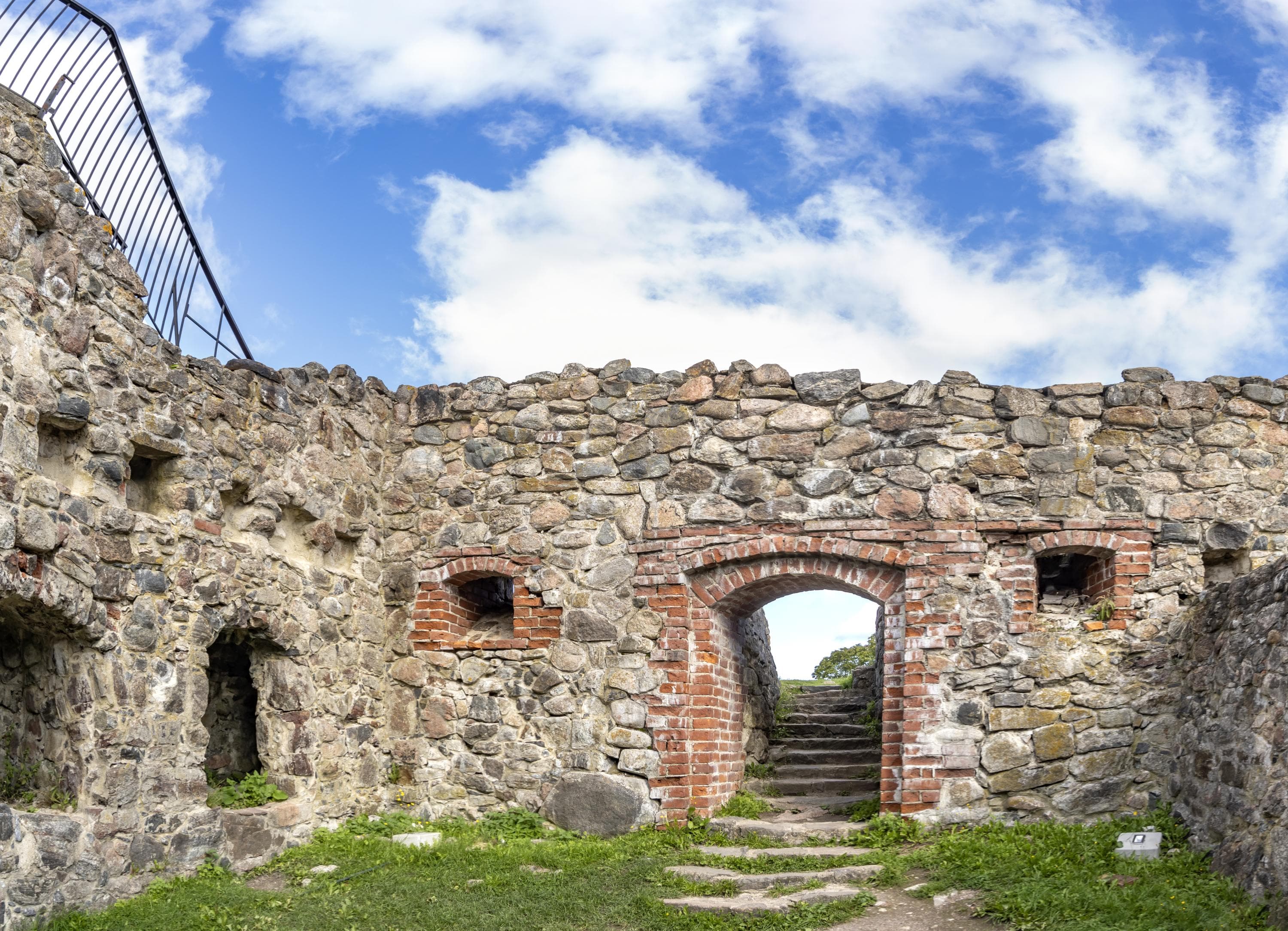 Kuva: Jari Kostet Linnan raunioissa on muurattu oviaukko ja kaksi ikkunaa. Vasemmalla seinässä on aukkoja ja päällä kaide. Taustalla taivaalla pilvenhattaroita.