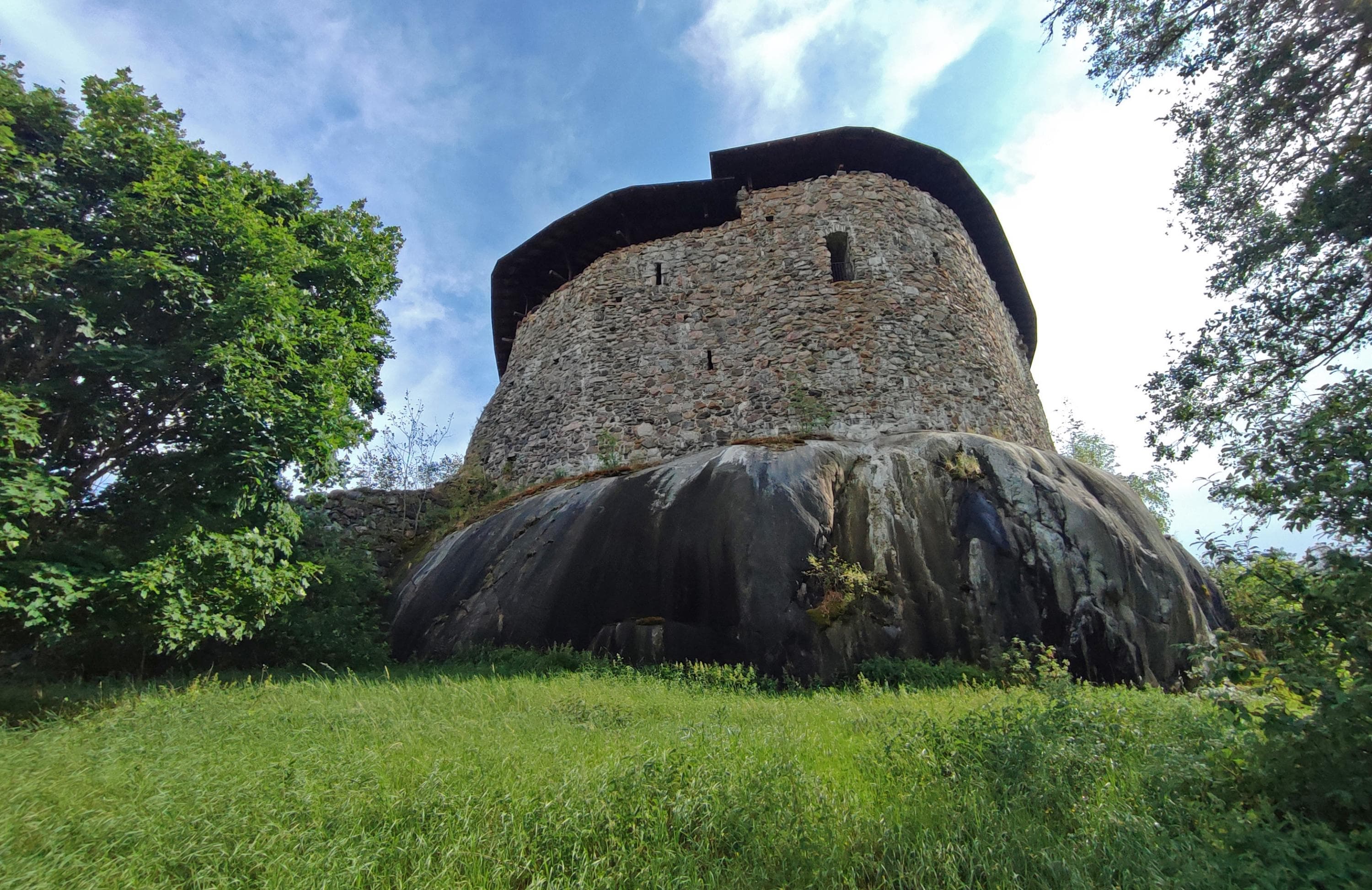 Kuva: Jussi Helimäki Linna kohoaa kallion päällä. Etualla nurmea ja puita.